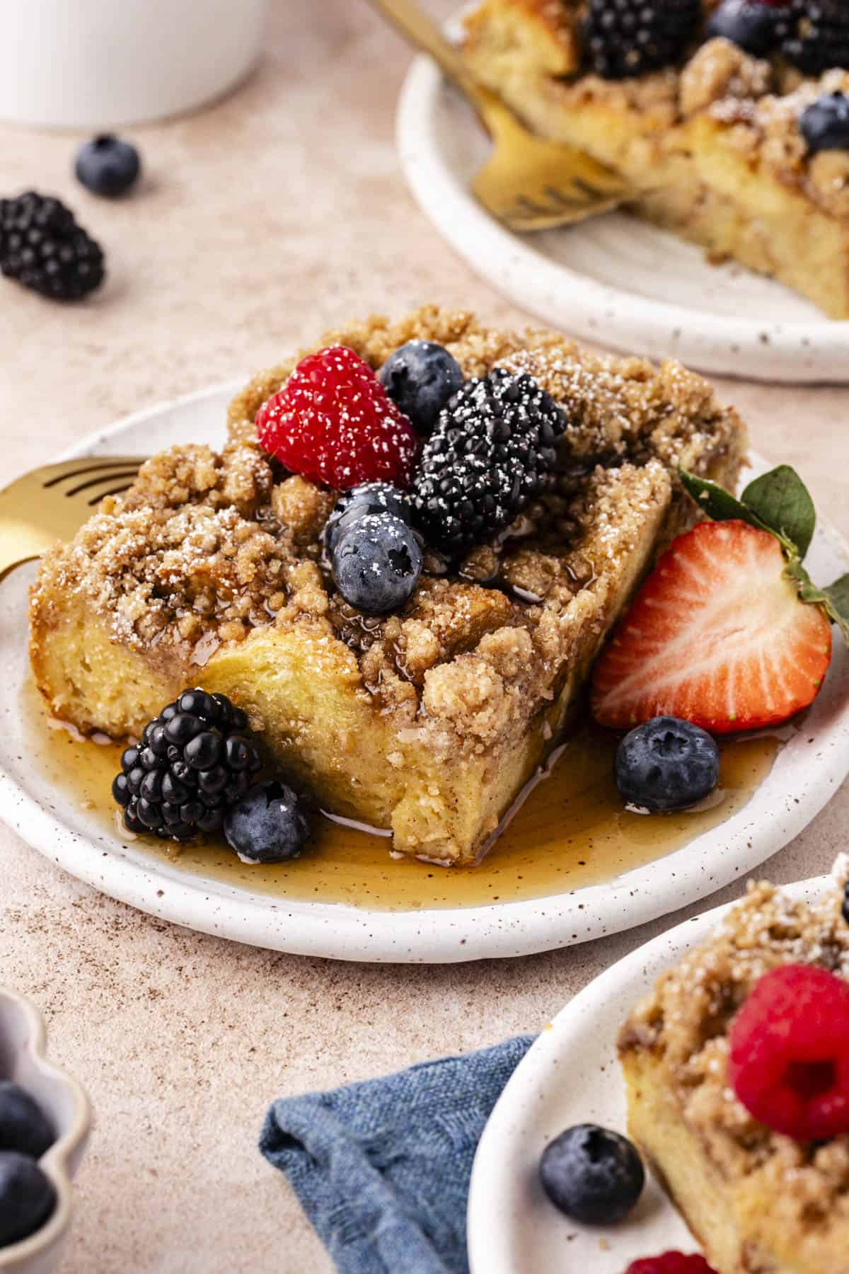 three small plates with slices of french toast casserole on them topped with maple syrup, fresh berries, and a light dusting of powdered sugar