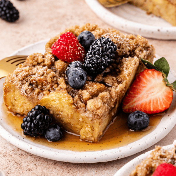 a slice of french toast casserole on a small plate with maple syrup and fresh berries