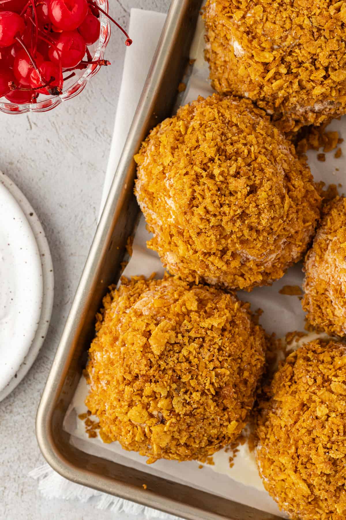 fried ice cream balls in rows on a sheet pan beside a small plate and a bowl of cherries