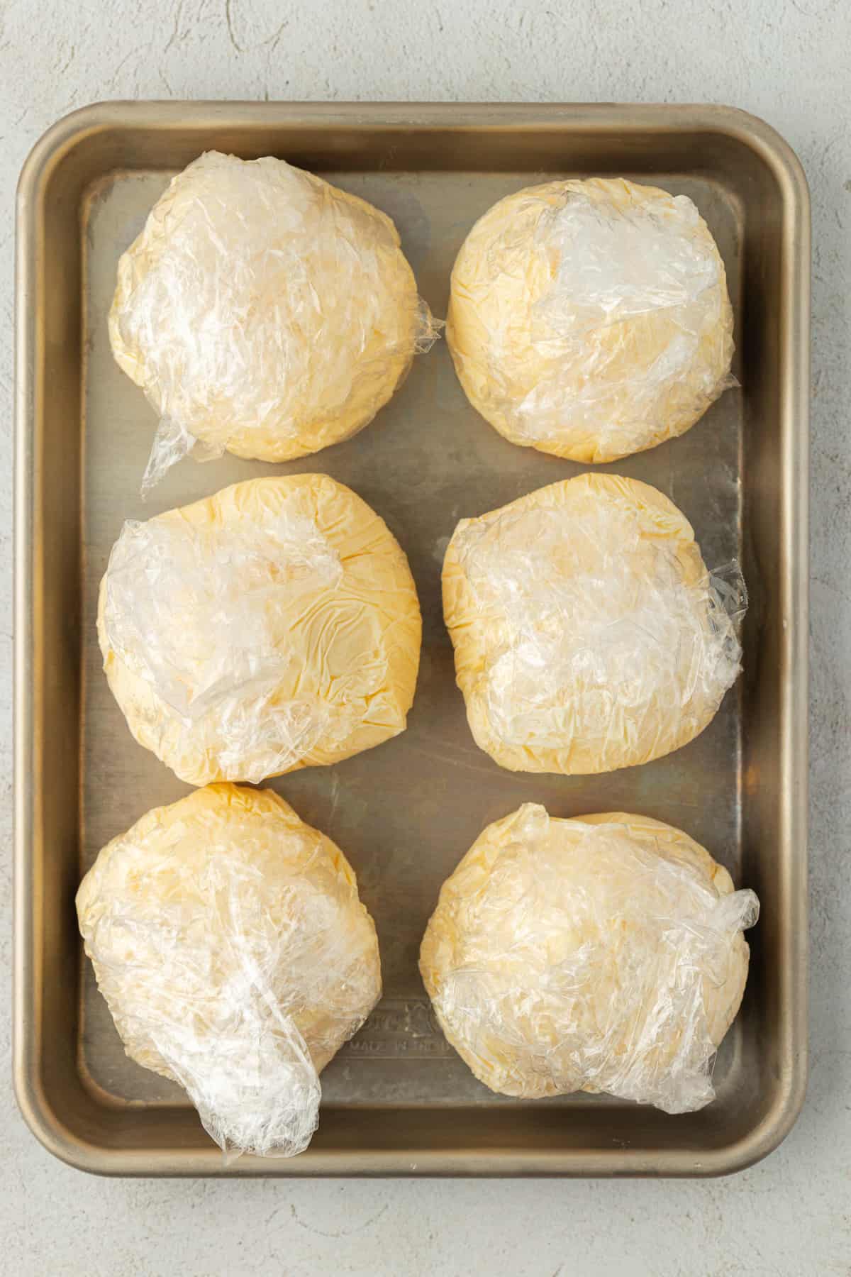 balls of vanilla ice cream wrapped in plastic wrap in two rows of three on a sheet pan