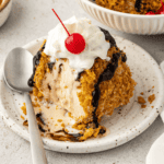 fried ice cream on a white plate with a spoon, topped with a cherry and whipped cream