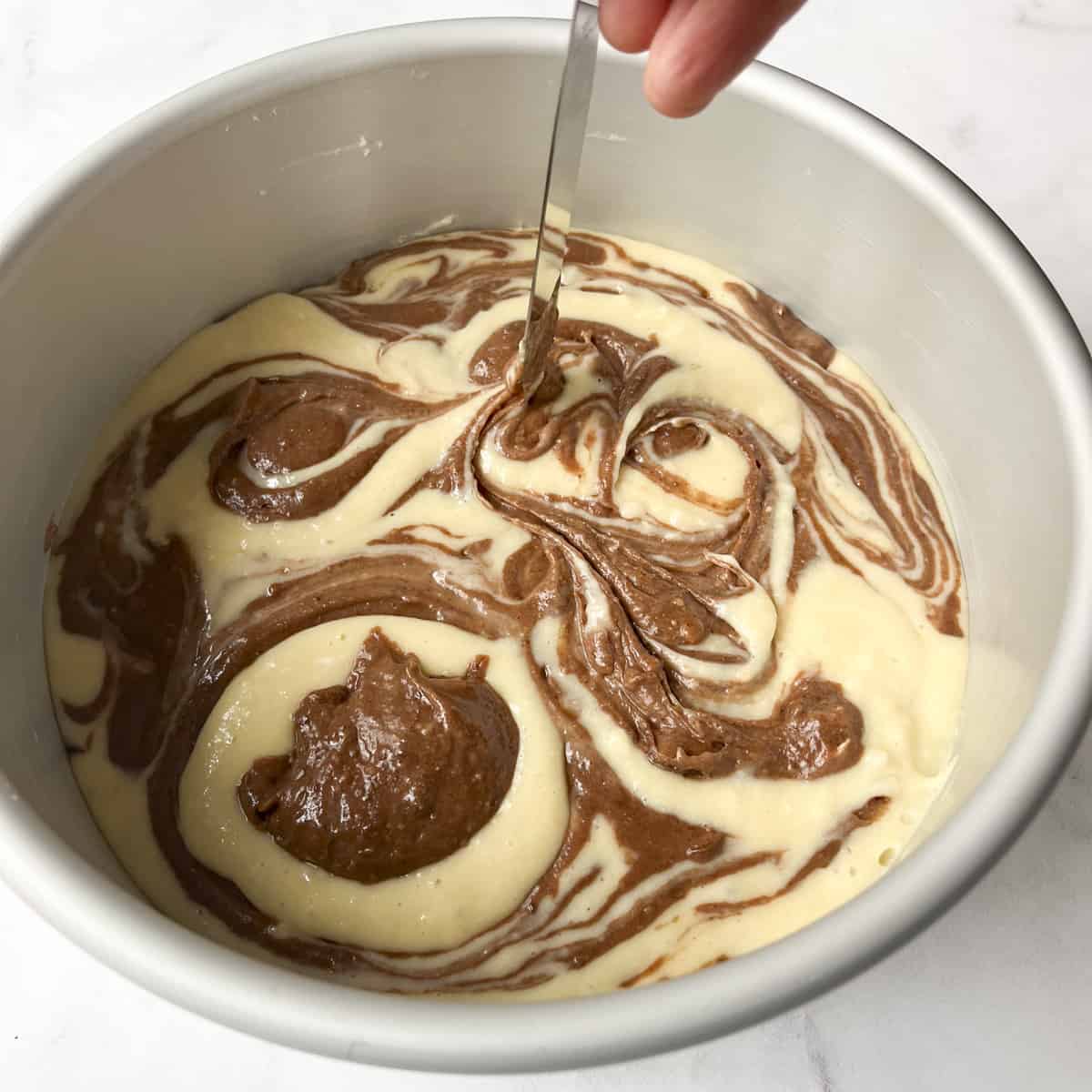 vanilla and chocolate cake batter being swirled with a knife in a cake pan