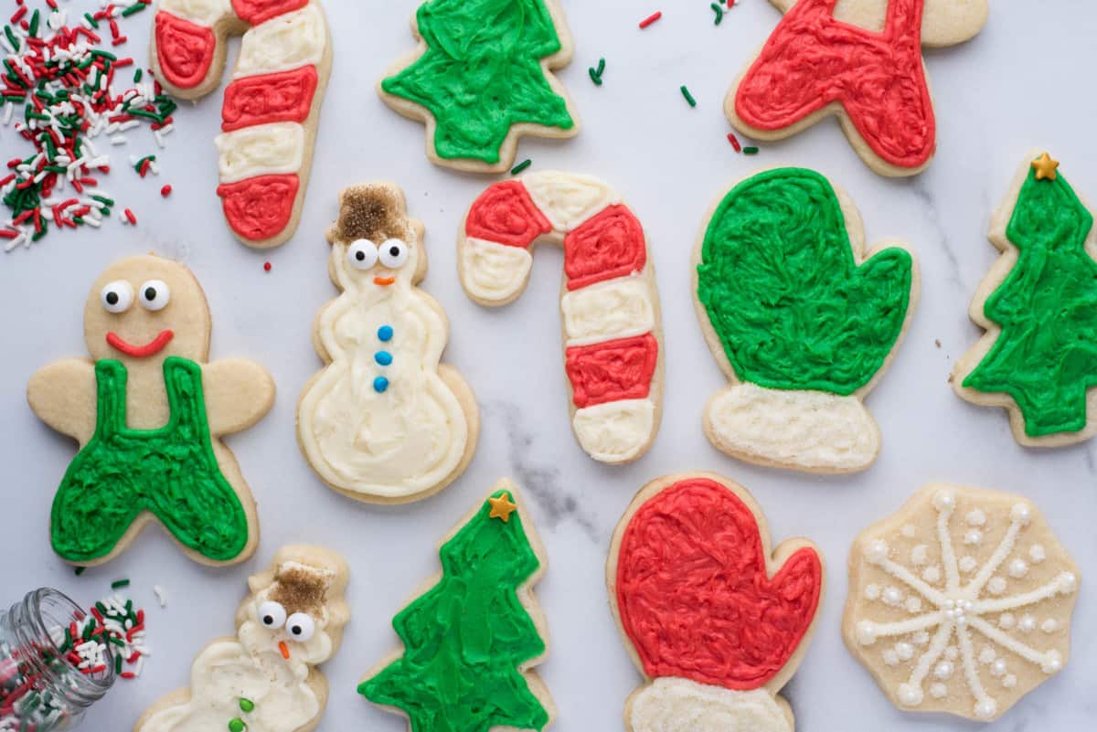an assortment of christmas sugar cookies in different shapes including a snowman, candy canes, christmas trees and snow mits