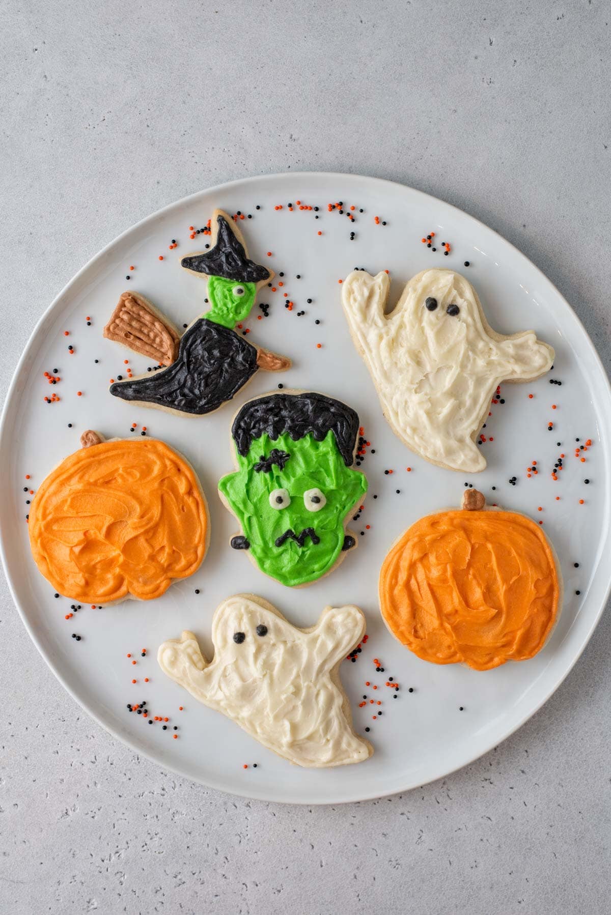 a plate with assorted halloween sugar cookies including pumpkins, ghosts, witch, and frankenstein