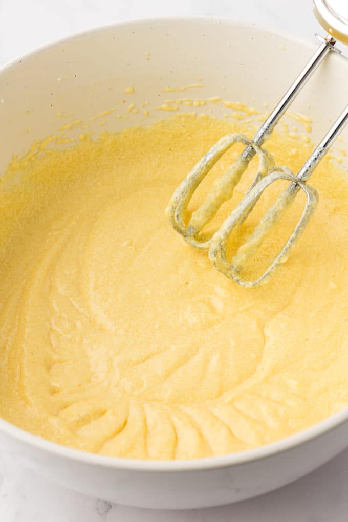 wet ingredients for vanilla bundt cake in a white bowl with the whisks of an electric mixer leaning inside the bowl
