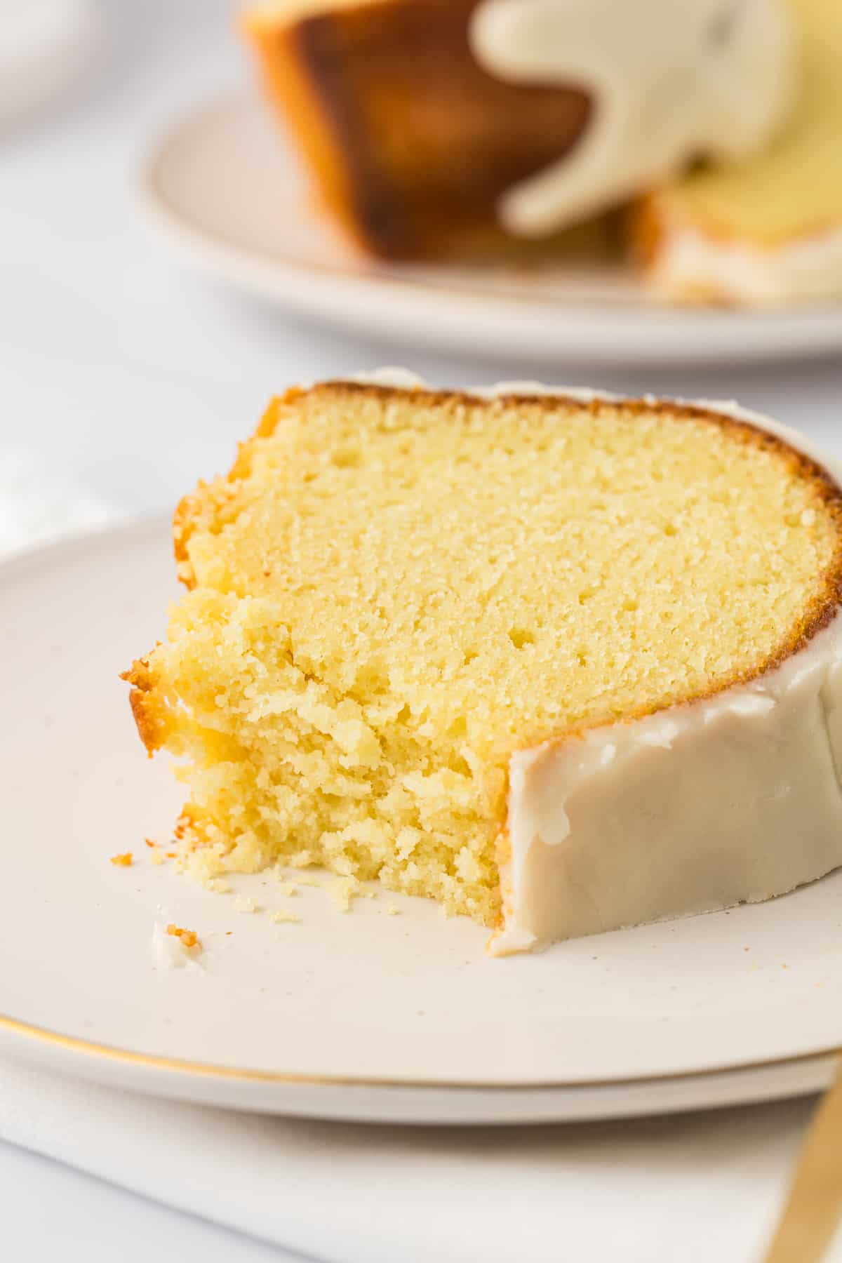 a slice of vanilla bundt cake on a small white plate with a bite missing out of it