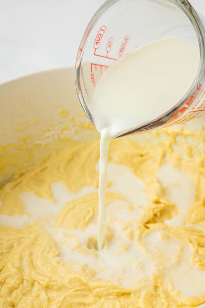 batter for vanilla bundt cake in a white bowl with a measuring cup of milk being poured on top