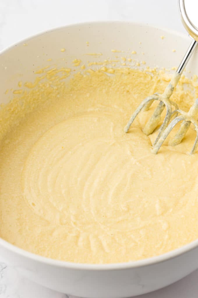 batter for vanilla bundt cake in a white bowl with the whisks of an electric mixer leaning inside the bowl