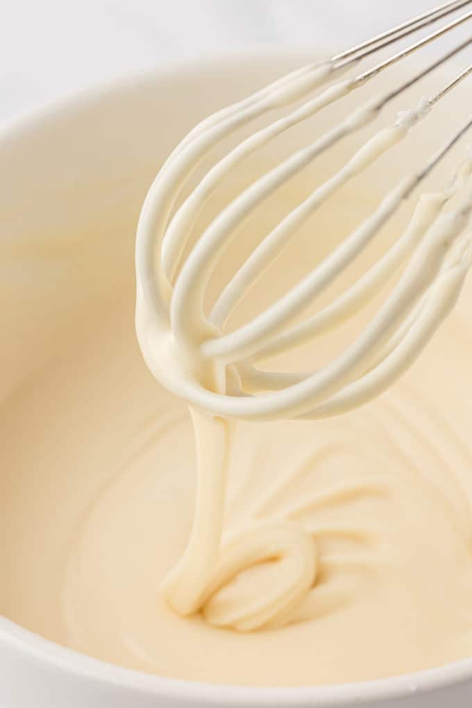 vanilla glaze being drizzled off a wire whisk into a white bowl full of glaze