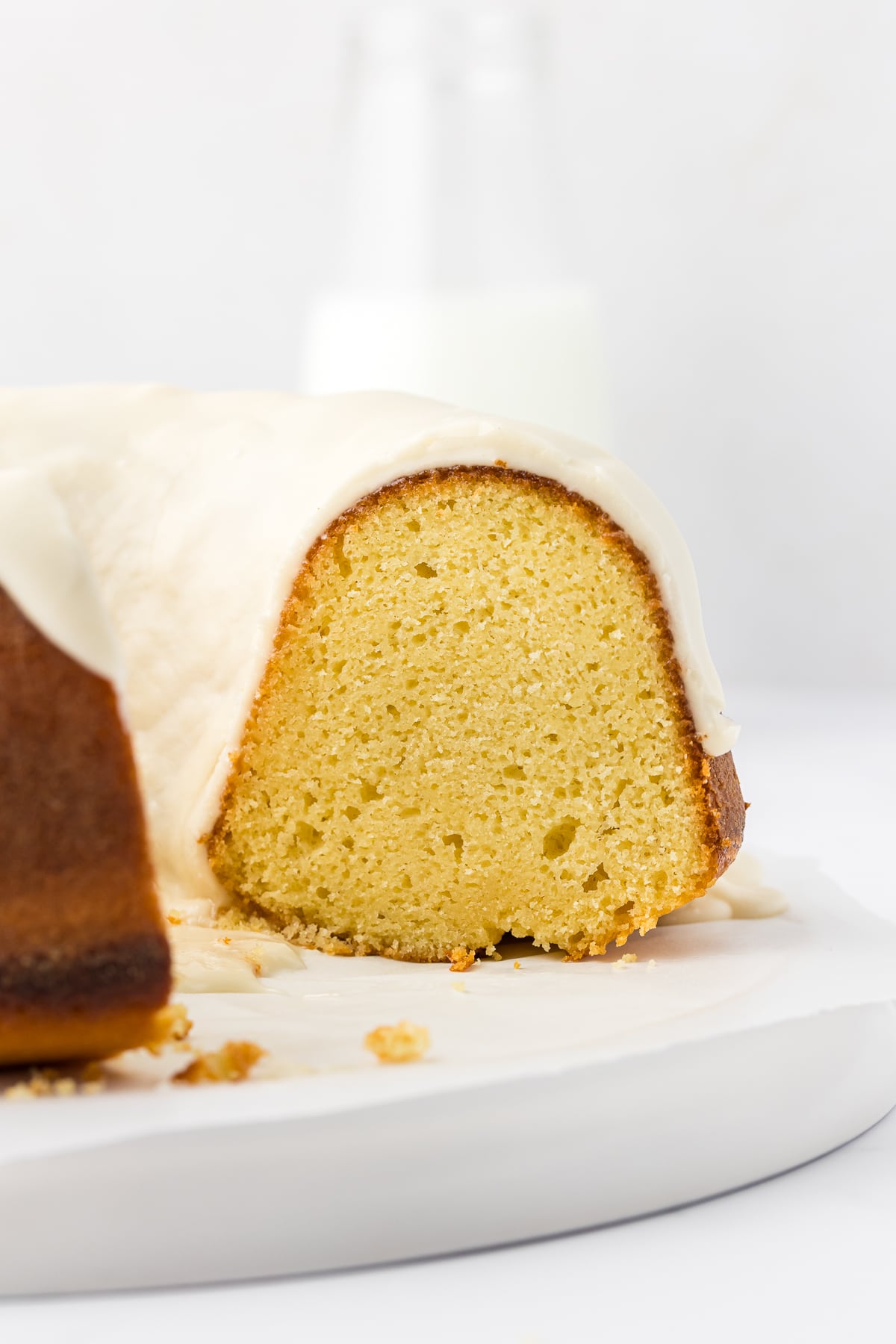 side view of a vanilla bundt cake with slices missing, exposing the inside of the cake with the glaze layer on top
