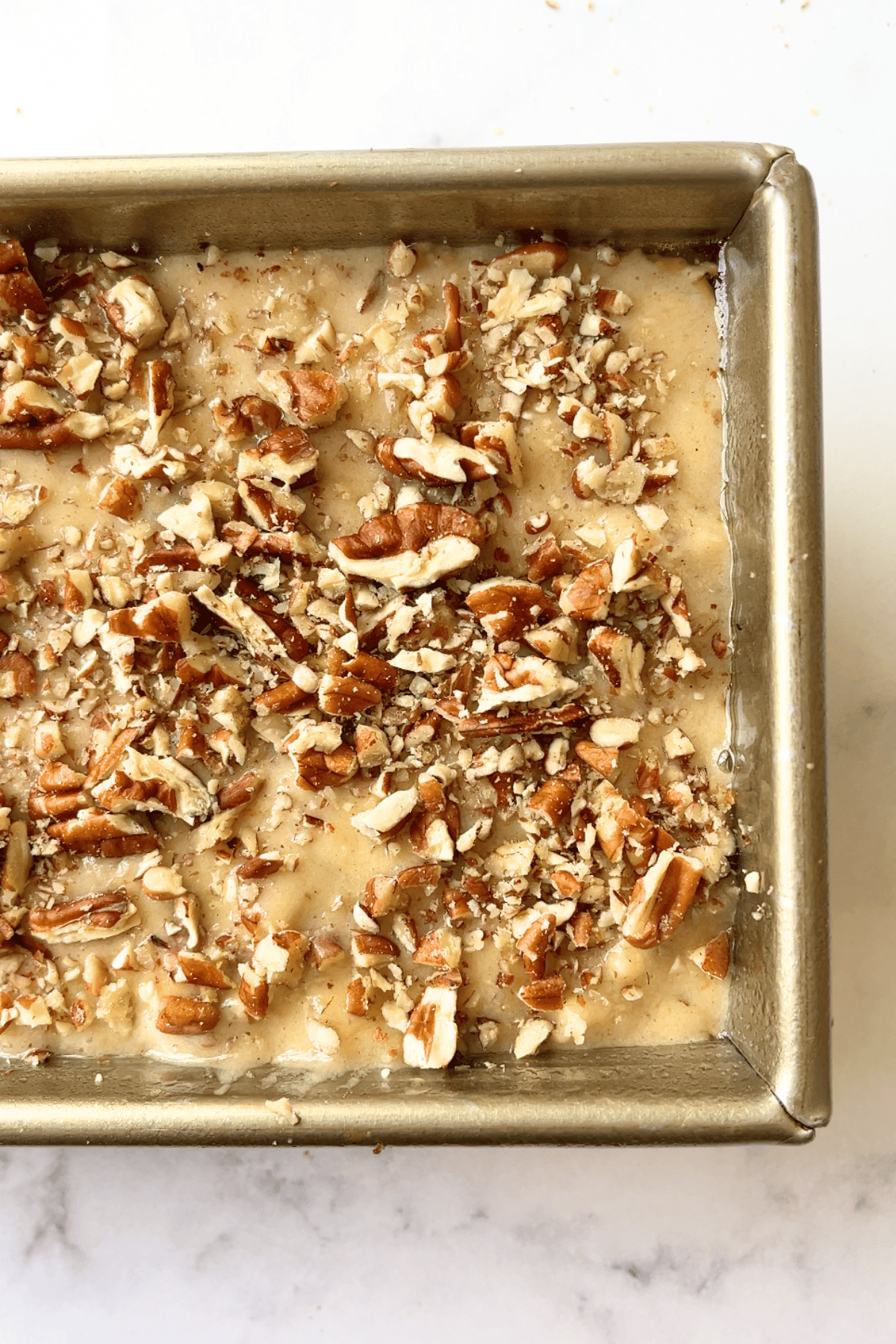 banana nut bread batter in a loaf pan topped with chopped pecans