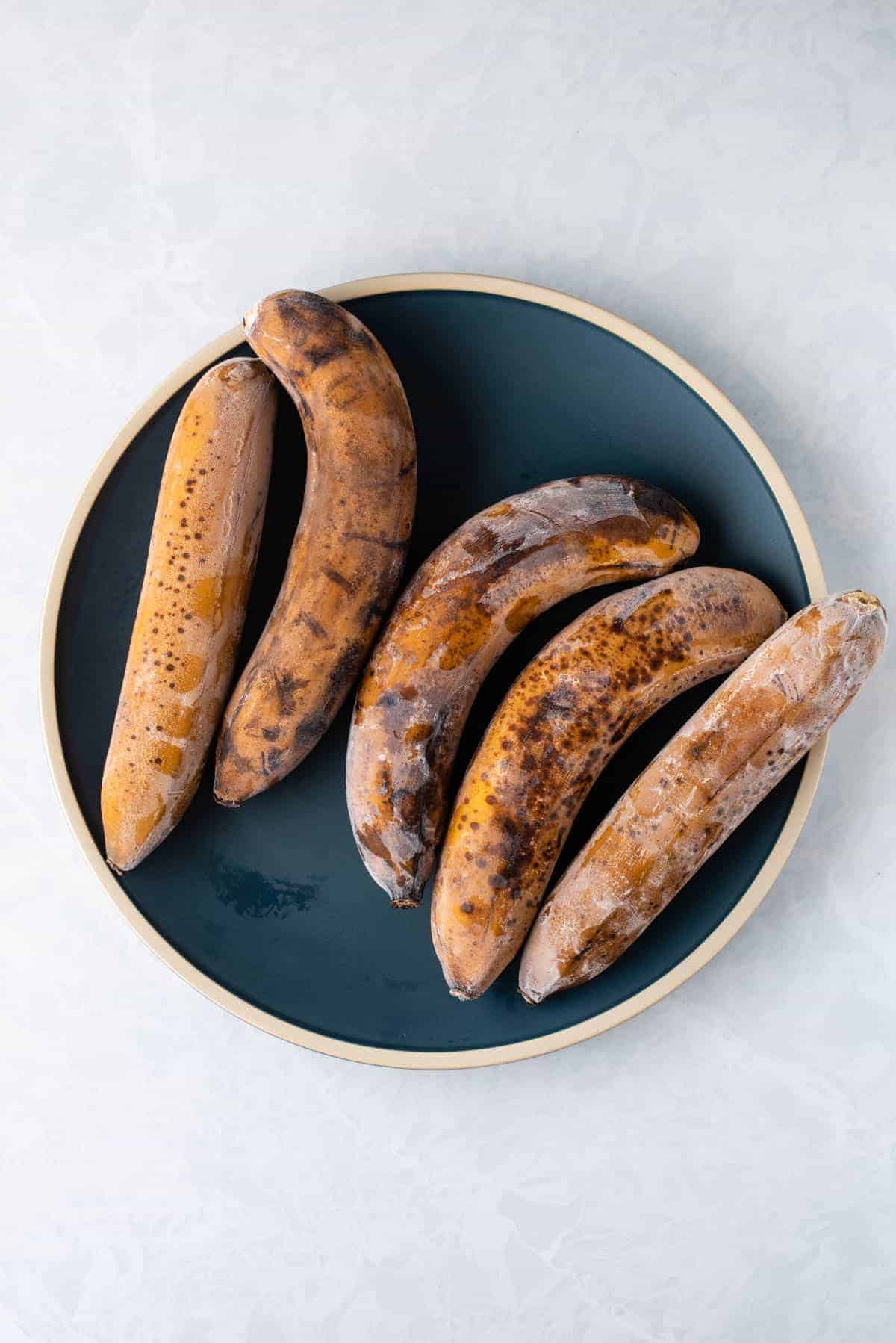 five whole frozen extra ripe bananas on a dark blue plate