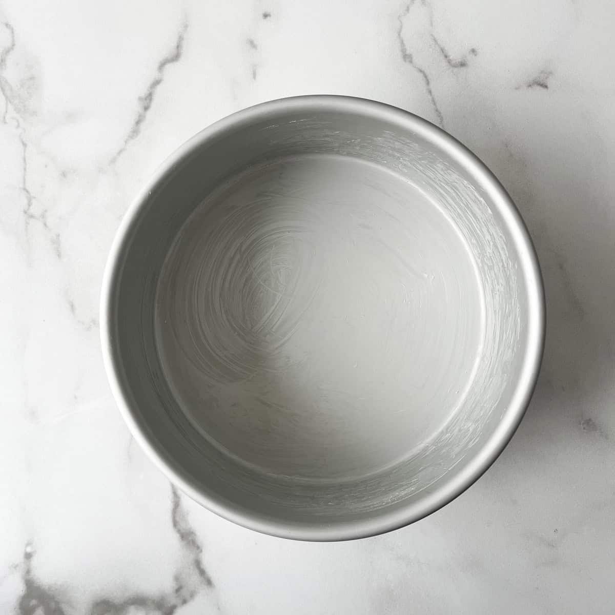a round cake pan greased with butter sitting on a countertop