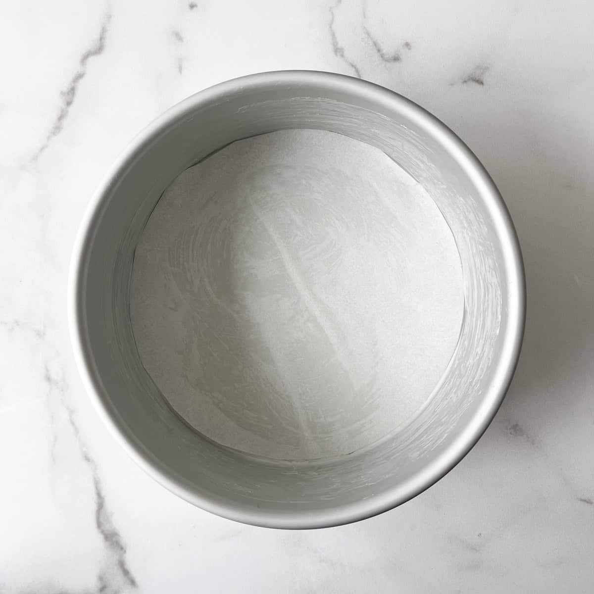 a round cake pan greased with butter with a round piece of parchment paper lining the bottom
