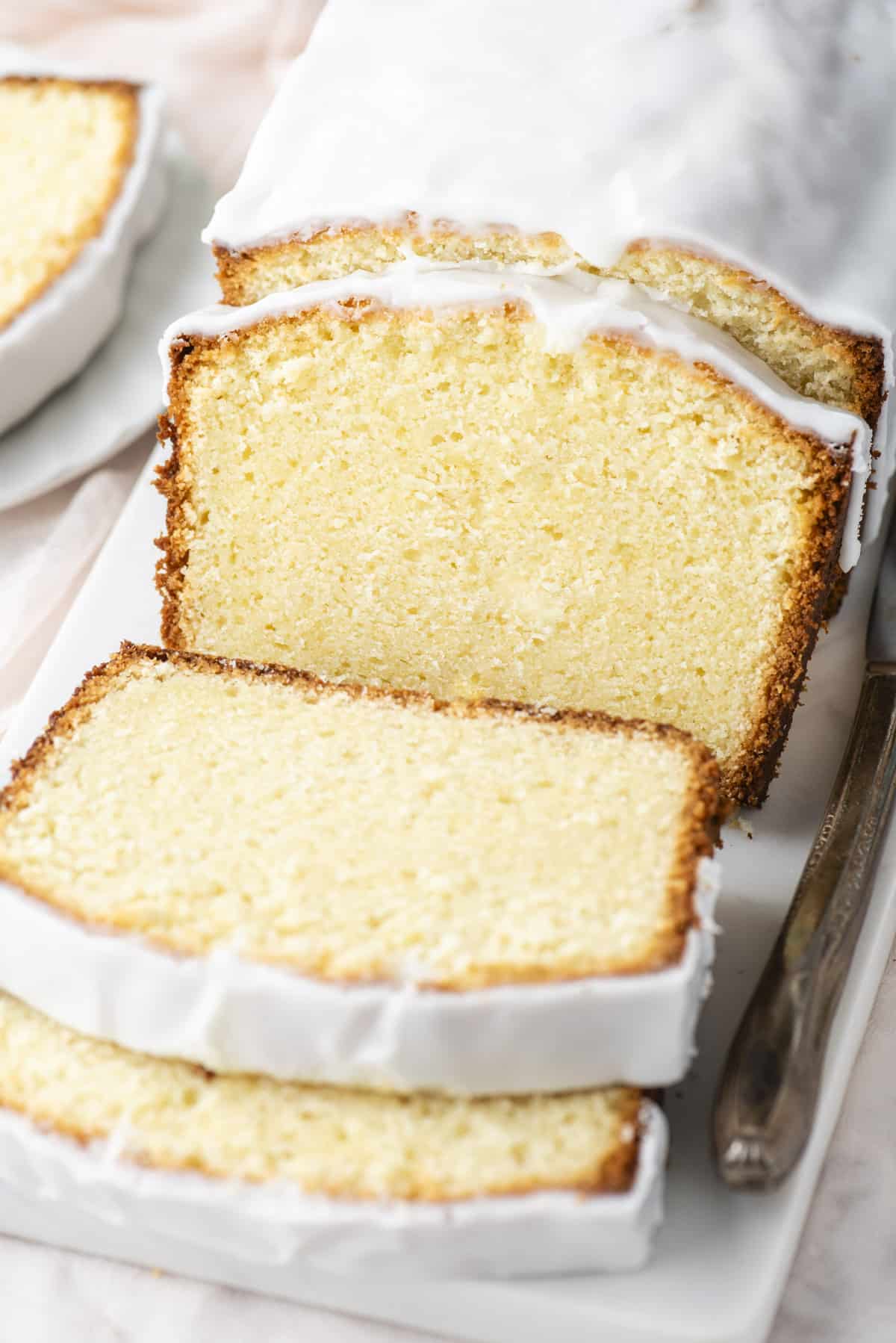 close up of slices of cream cheese pound cake on a white cutting board with a white plate with one slice of cake beside it
