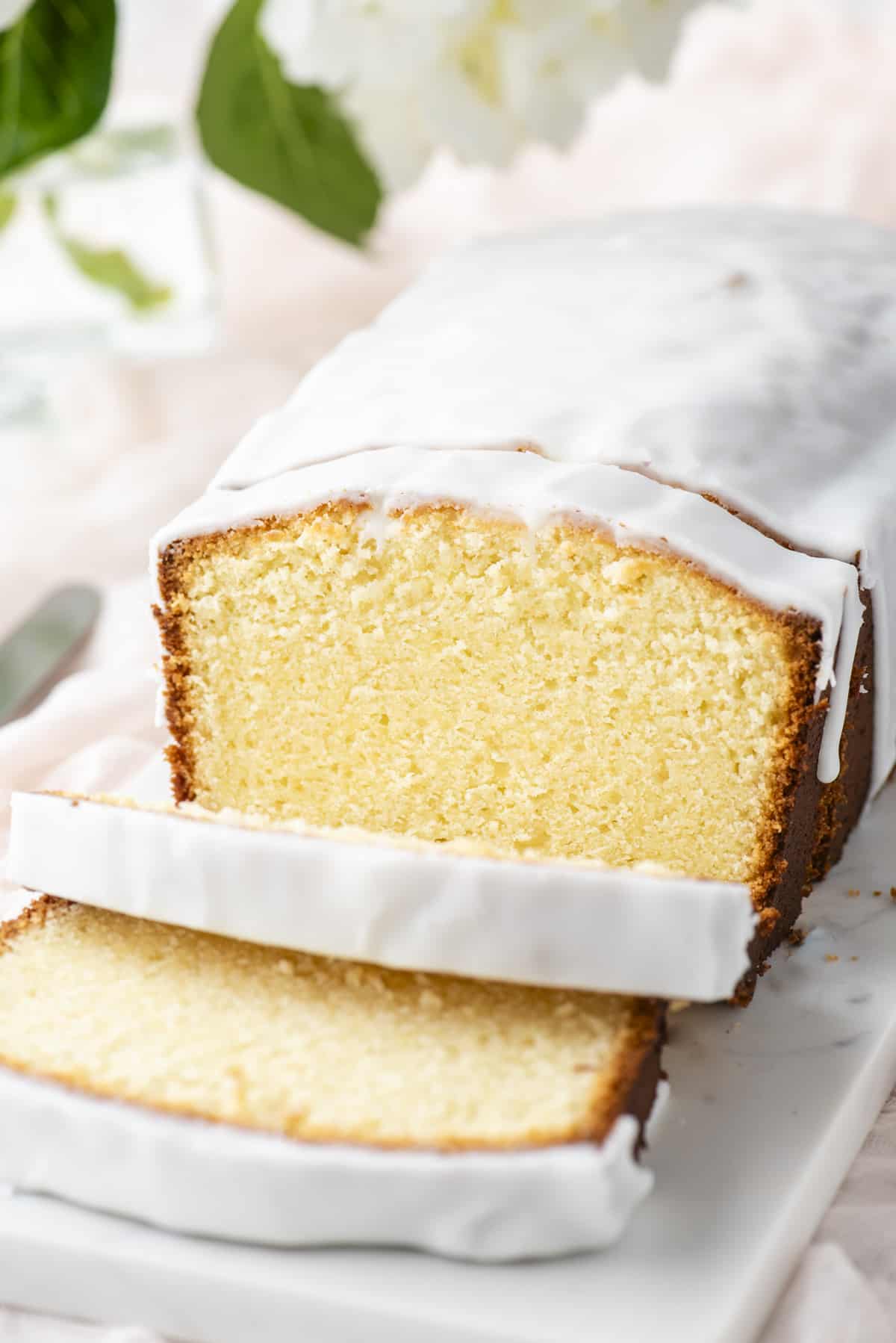 cream cheese pound cake with three slices cut on a white cutting board