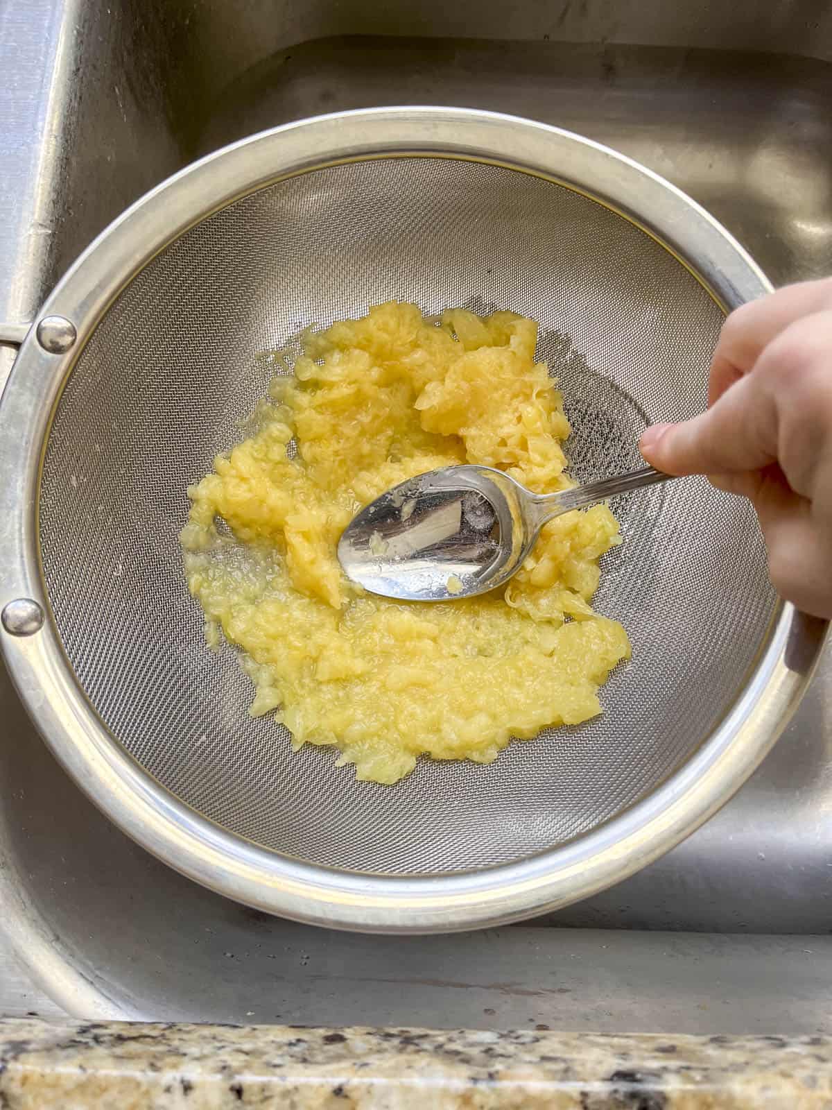 crushed pineapple in a fine mesh strainer being pressed with a spoon