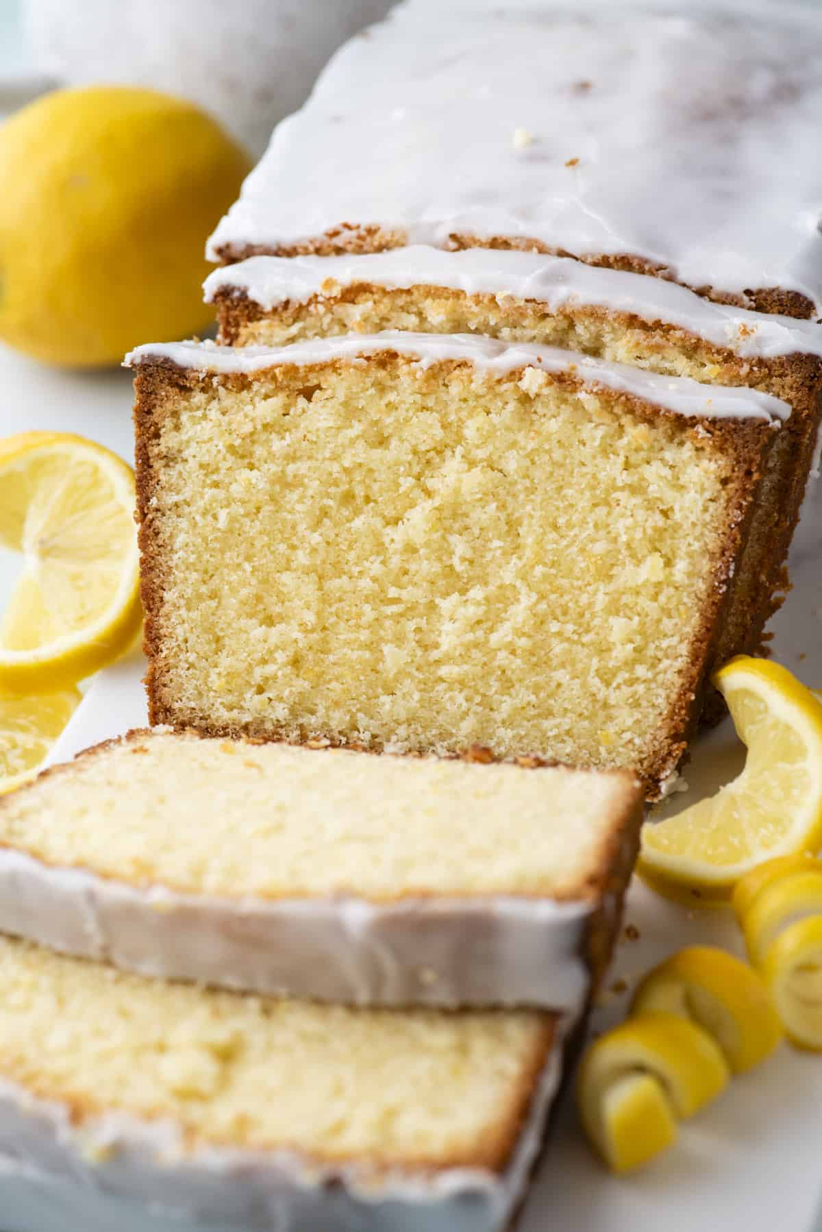 a sliced lemon pound cake surrounded by fresh lemon slices and lemon peels