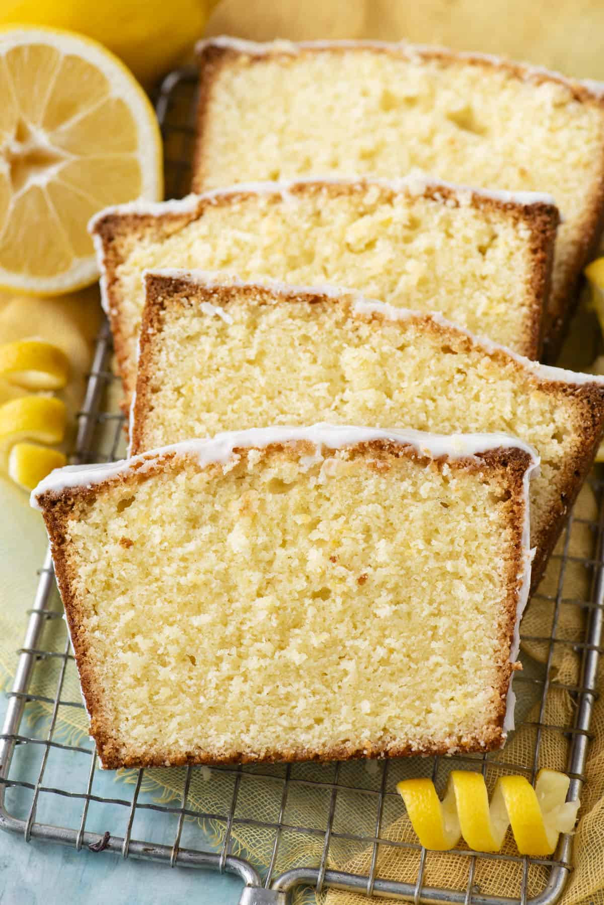 slices of lemon pound cake on a wire rack surrounded by lemon slices and peels