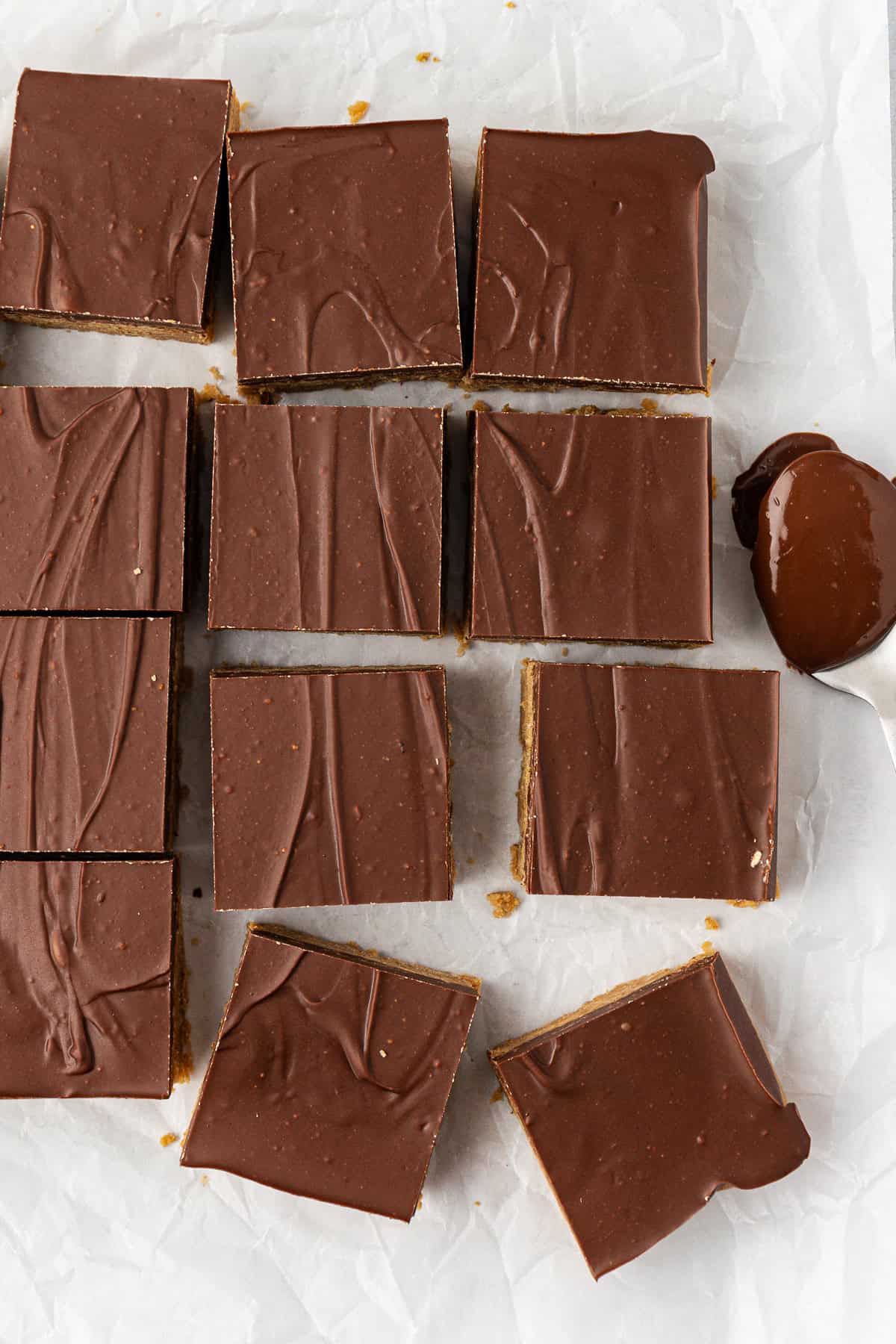 over head view of rows of peanut butter bars showing the top layer of chocolate with a spoon full of melted chocolate beside them