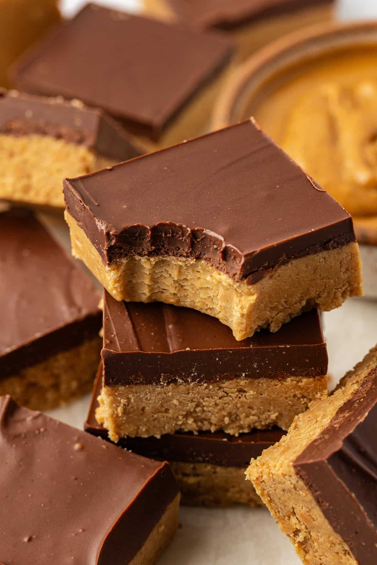a stack of three peanut butter bars with a bite out of the top bar and more peanut butter bars scattered all around