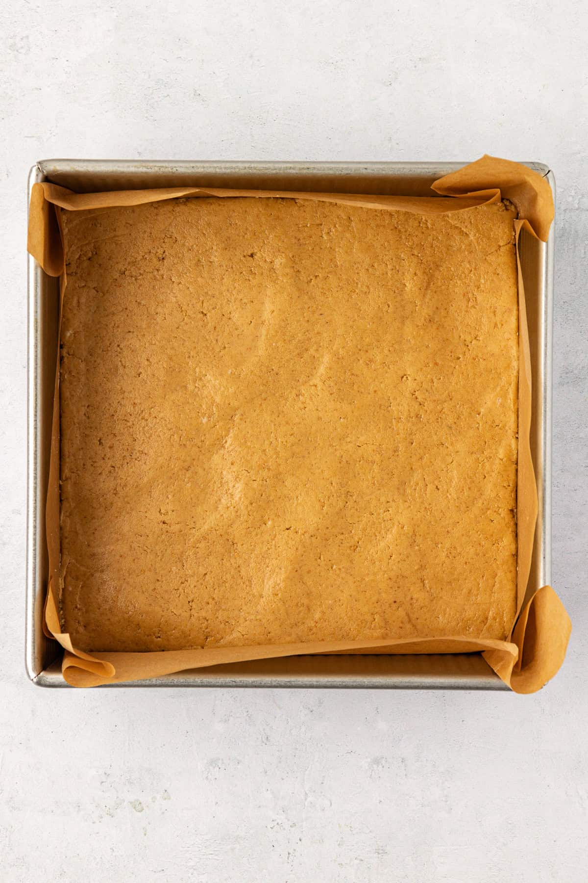a square pan lined with parchment paper with a smooth layer of peanut butter mixture in it