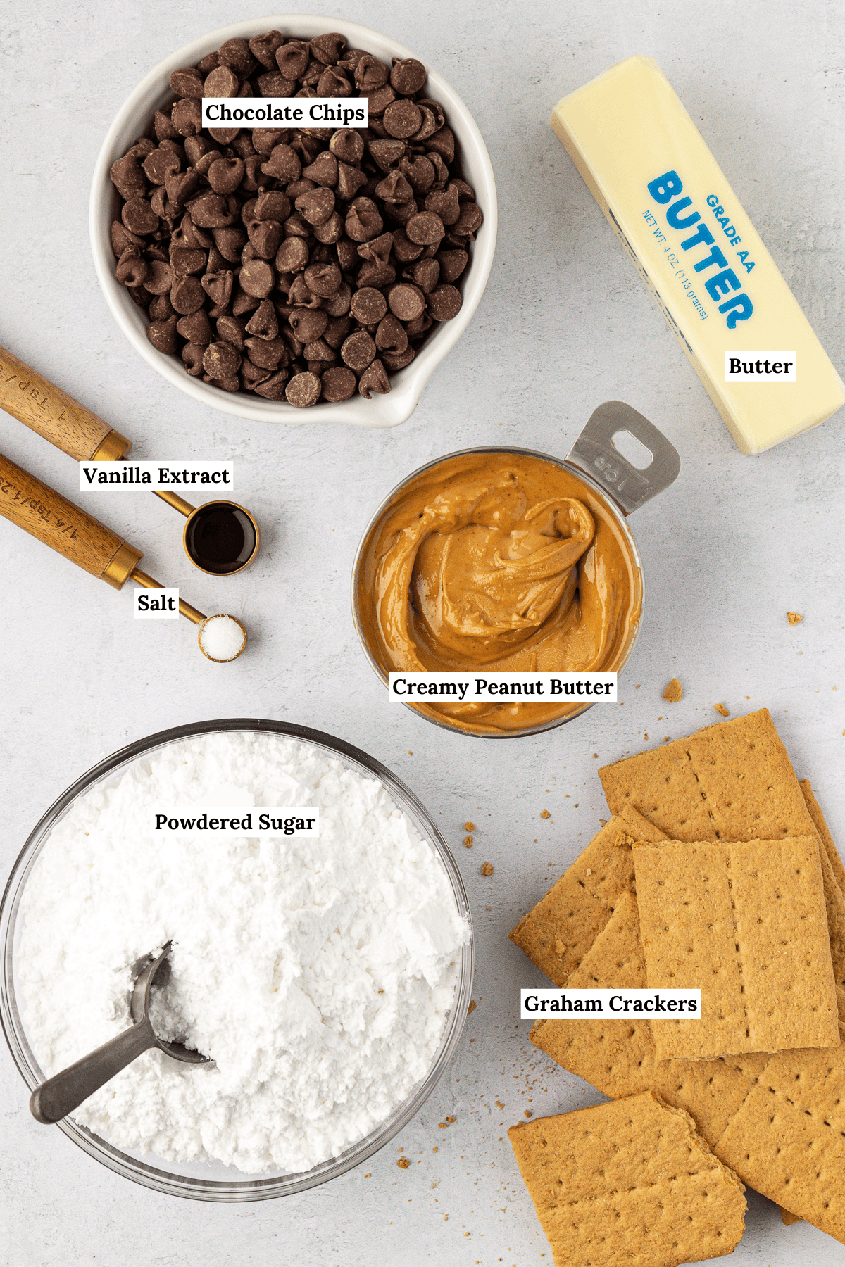 over head view of the ingredients for peanut butter bars including chocolate chips, a stick of butter, creamy peanut butter, vanilla extract, salt, powdered sugar, and graham crackers