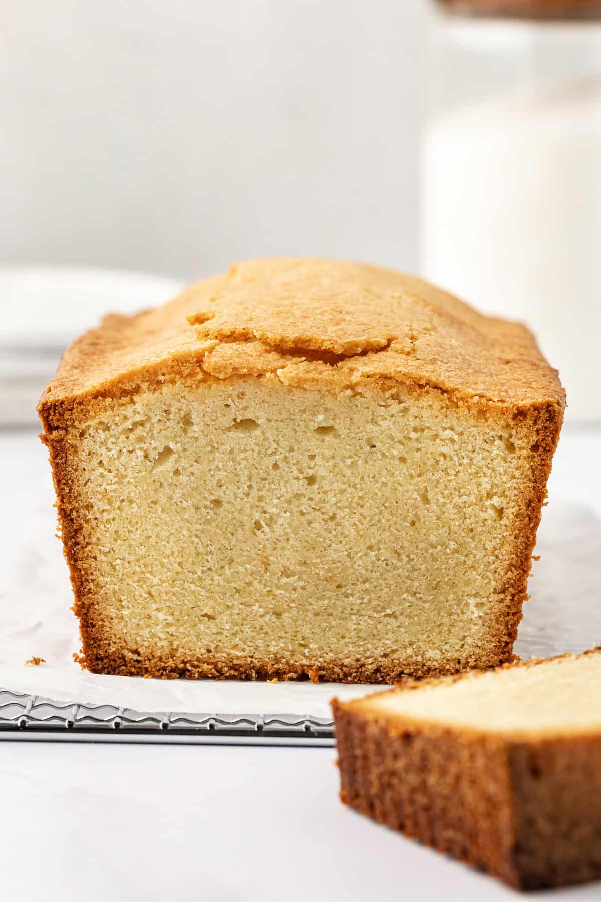 a pound cake on parchment paper on a wire rack with one slice cut sitting beside the cake, exposing the light yellow inside with a golden brown edge