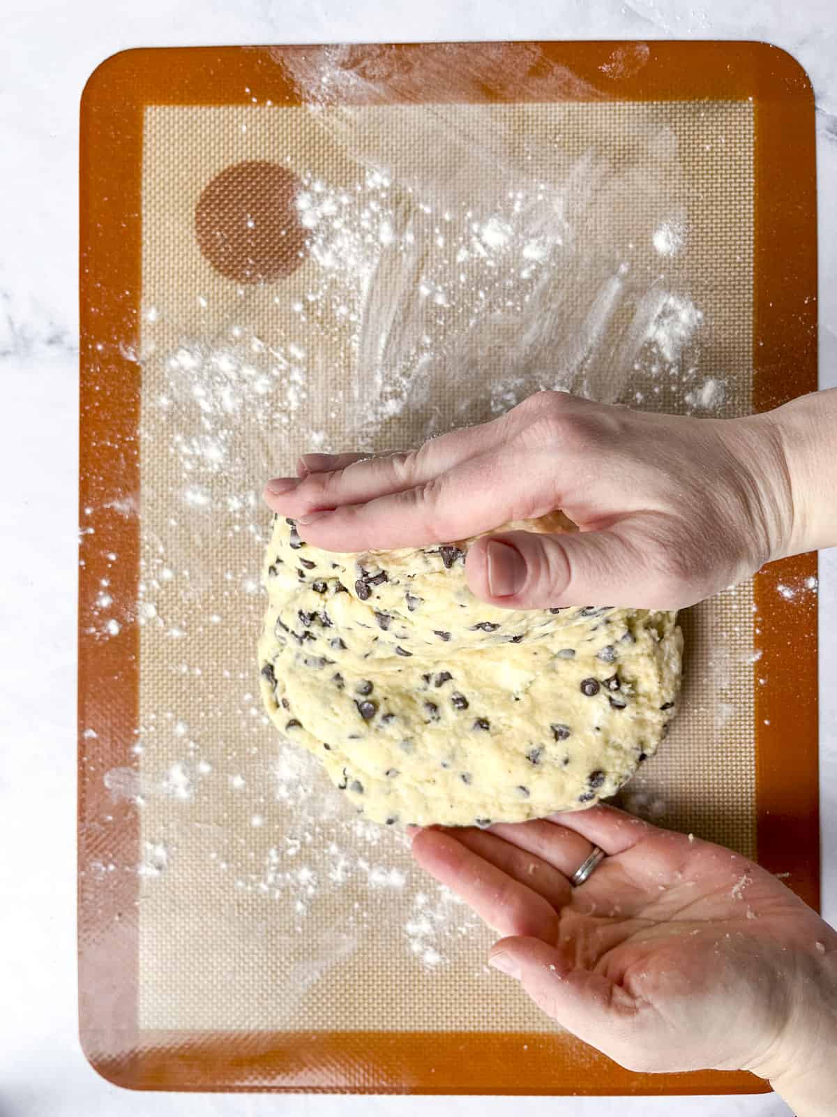 two hands folding scone dough on a silicone mat showing the lamination process