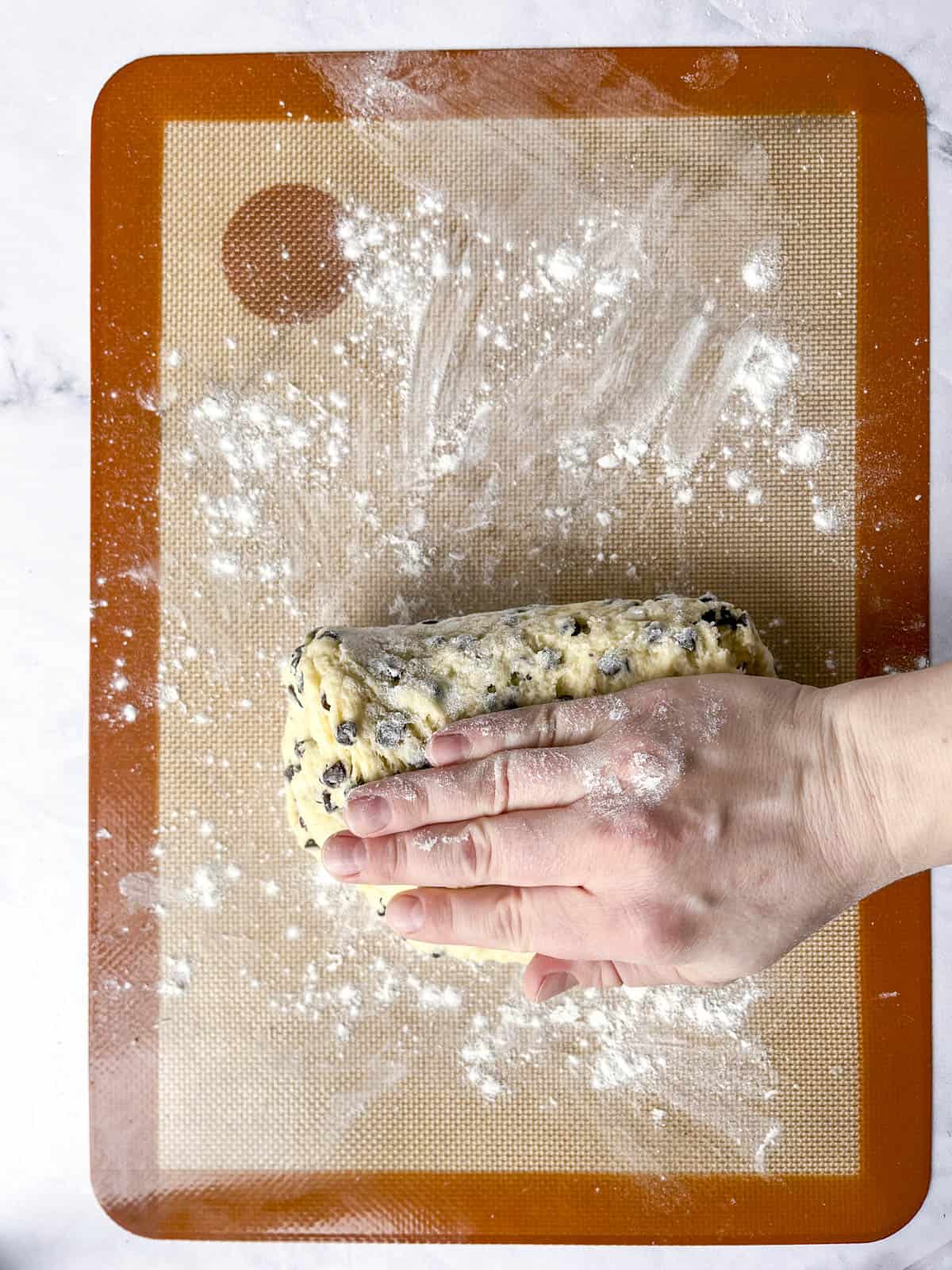 two hands folding scone dough on a silicone mat showing the lamination process