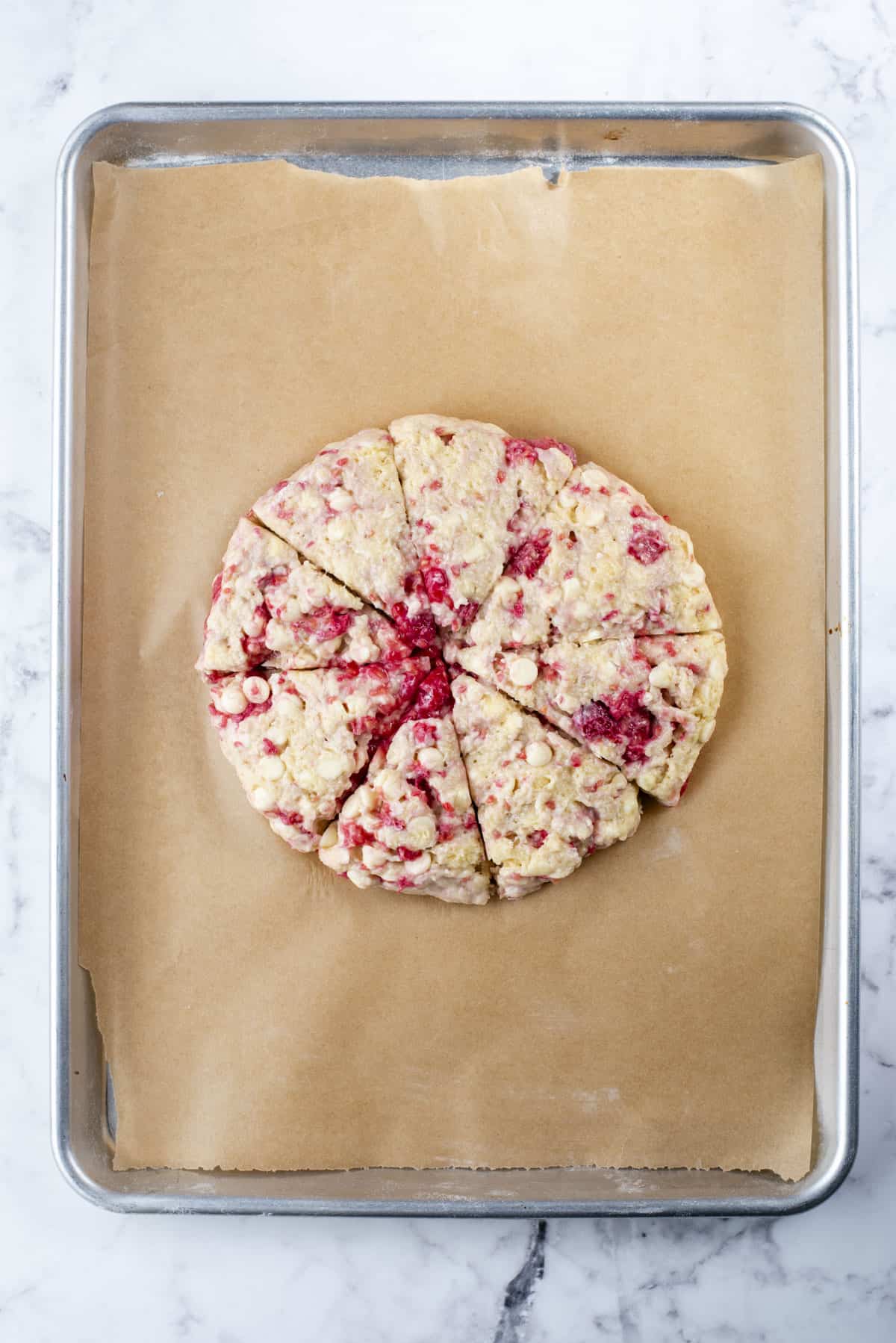 a round disc of raspberry white chocolate chip scone dough on a baking sheet lined with parchment paper