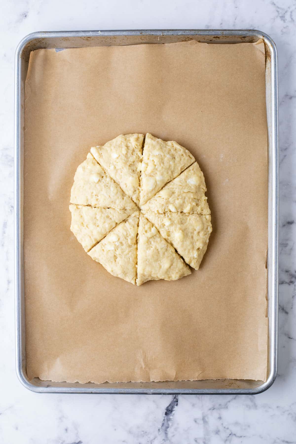 a round disc of scone dough sliced into wedges on a baking sheet lined with parchment paper
