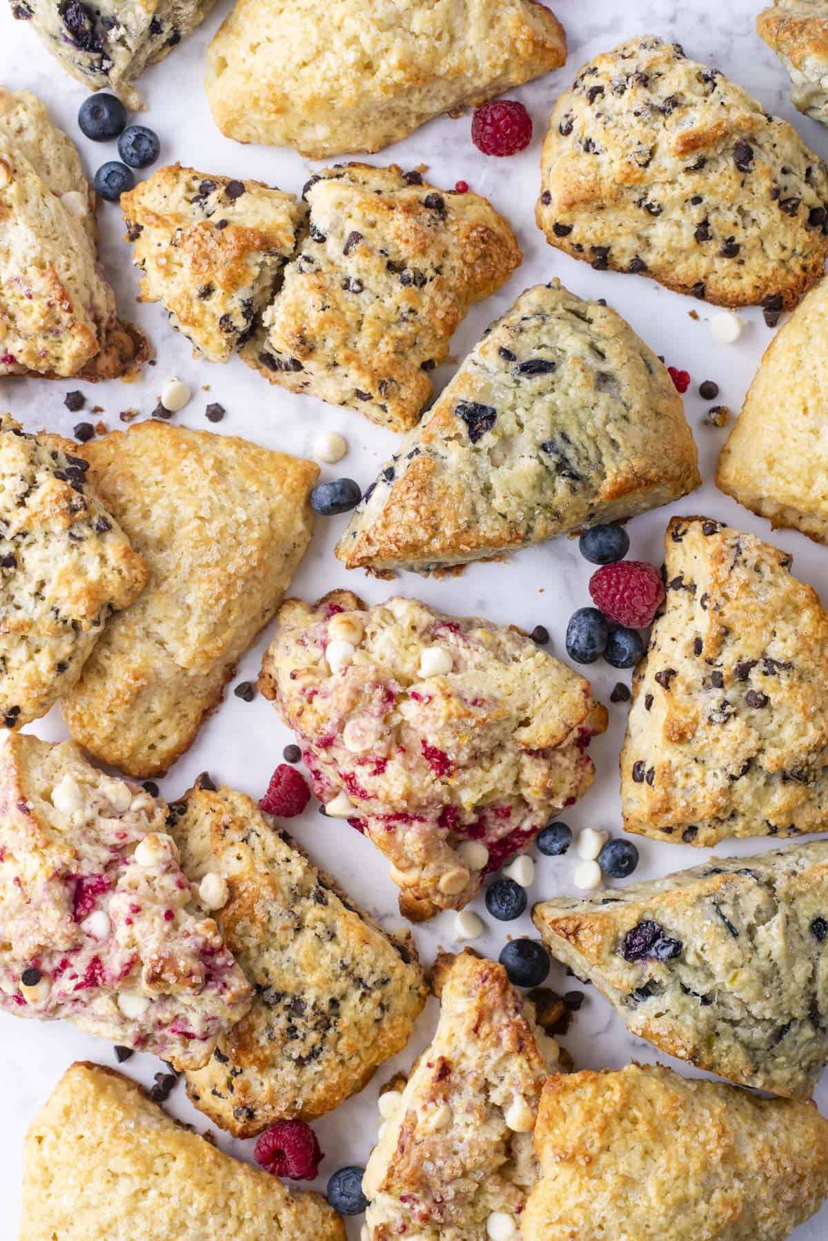 an assortment of scone flavors with fresh blueberries, raspberries and mini regular and white chocolate chips scattered around