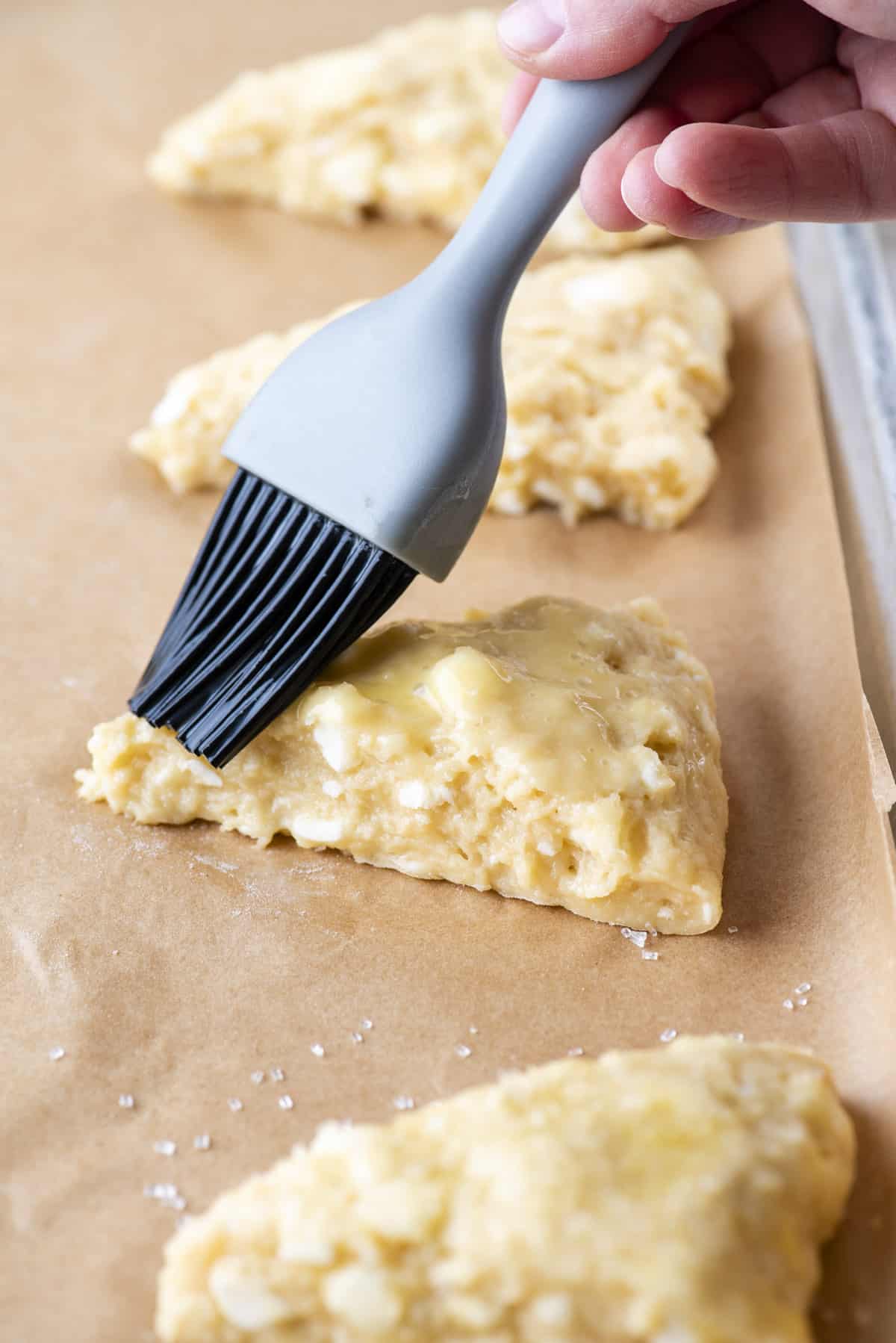 brushing scones with egg wash on a baking sheet lined with parchment paper
