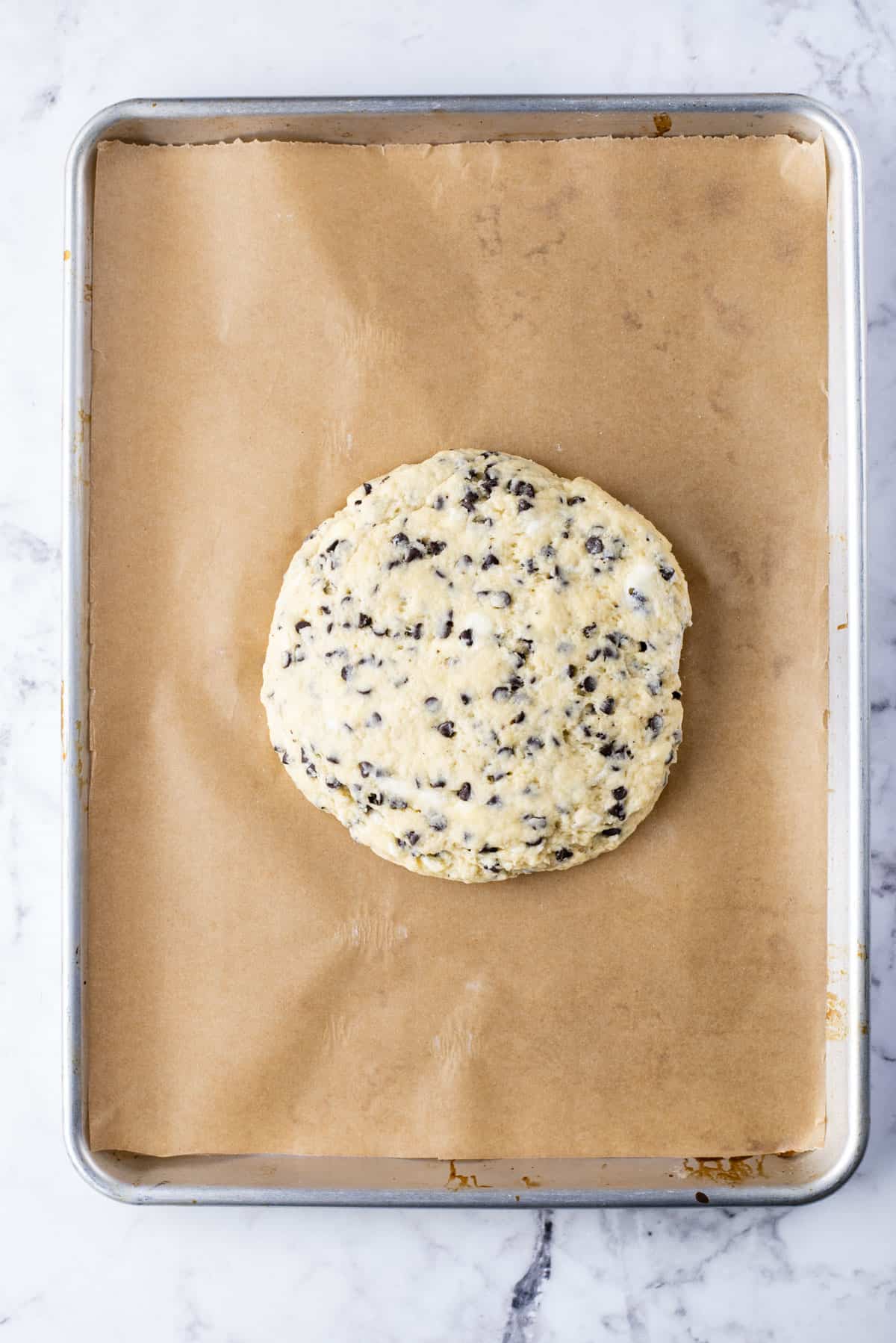 a round disc of chocolate chip scone dough on a baking sheet lined with parchment paper