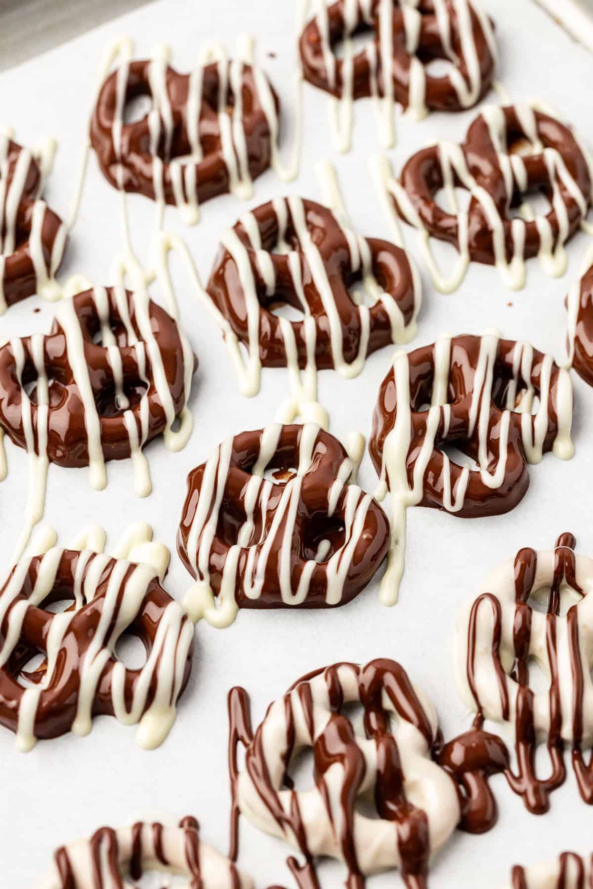 rows of twist pretzels on a baking sheet coating in chocolate and drizzled with white chocolate, with some rows coated in white chocolate and drizzled with chocolate