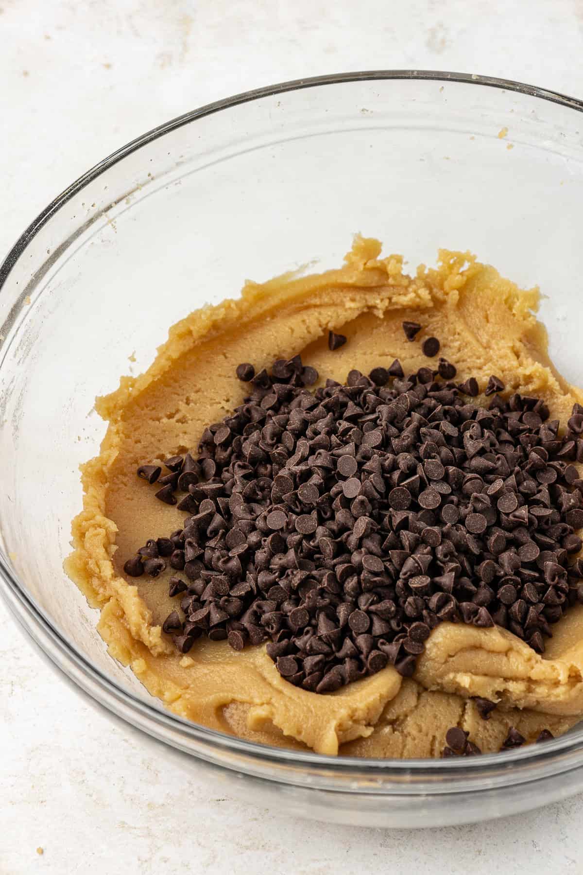 edible cookie dough in a clear glass bowl with a pile of chocolate chips on top