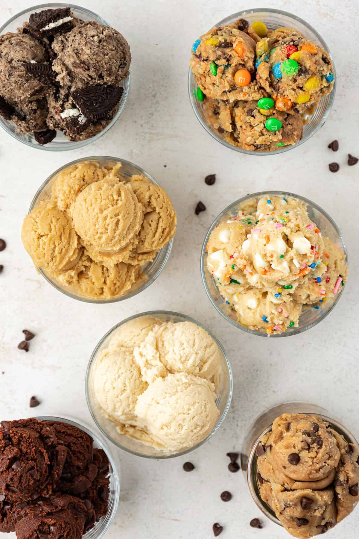 overhead view of seven clear class containers full of different cookie dough flavors including oreo, cookie monster, sugar cookie, peanut butter, funfetti, chocolate and chocolate chip