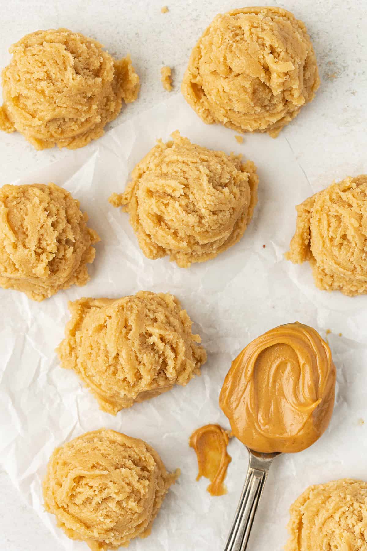 edible peanut butter cookie dough balls on white parchment paper with one spoon full of peanut butter