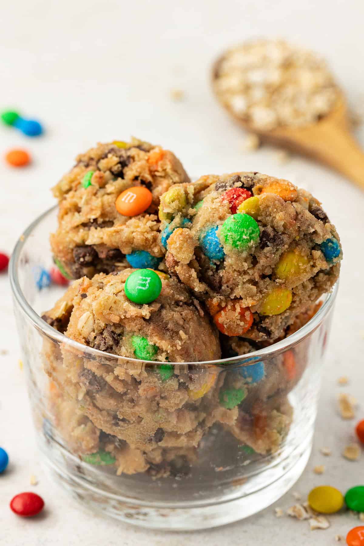 clear glass container of cookie monster cookie dough balls with oats and m&ms scattered around