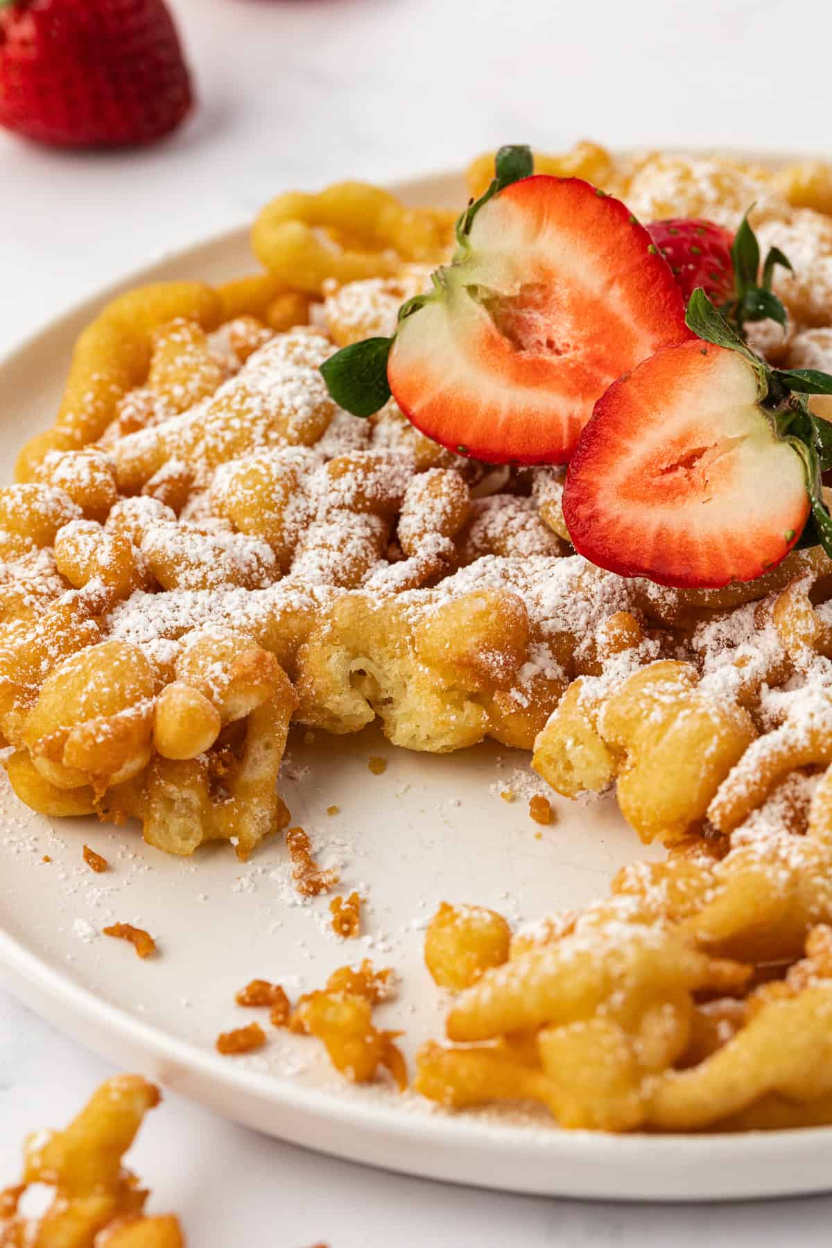 funnel cake on a white plate topped with powdered sugar and fresh strawberries
