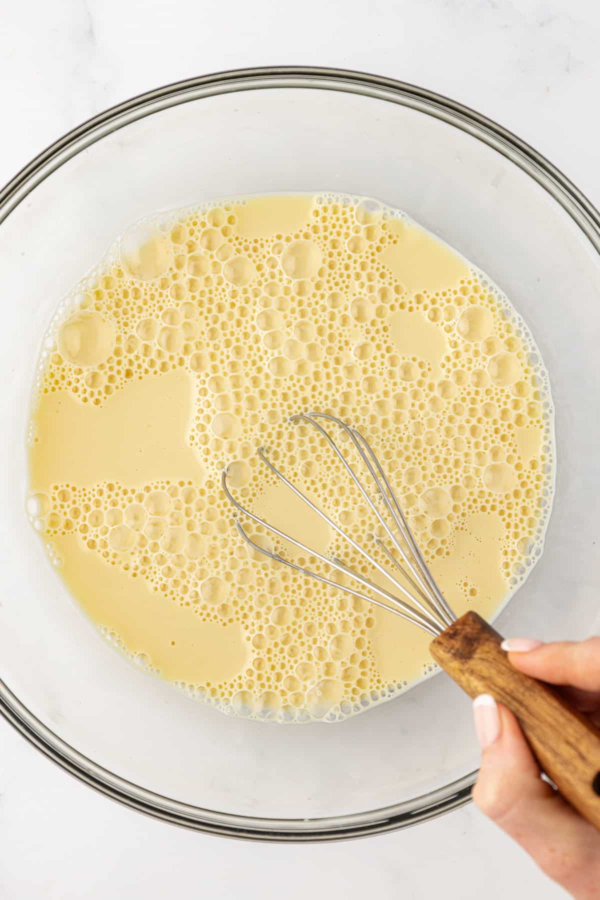 wet ingredients for funnel cake batter being whisked in a clear glass bowl