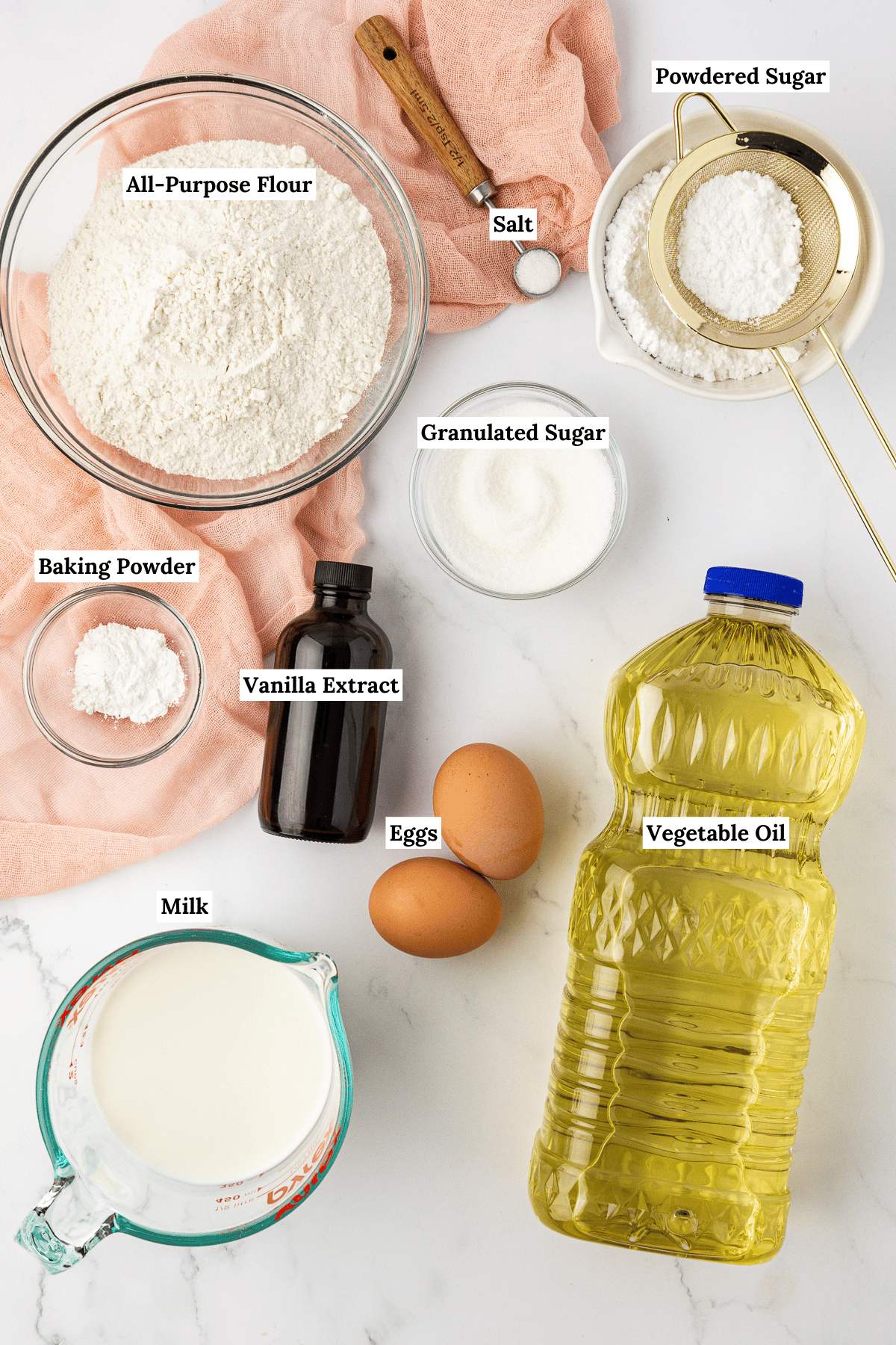 over head view of the ingredients for funnel cake including all-purpose flour, salt, powdered sugar, granulated sugar, baking powder, vanilla extract, eggs, vegetable oil and milk