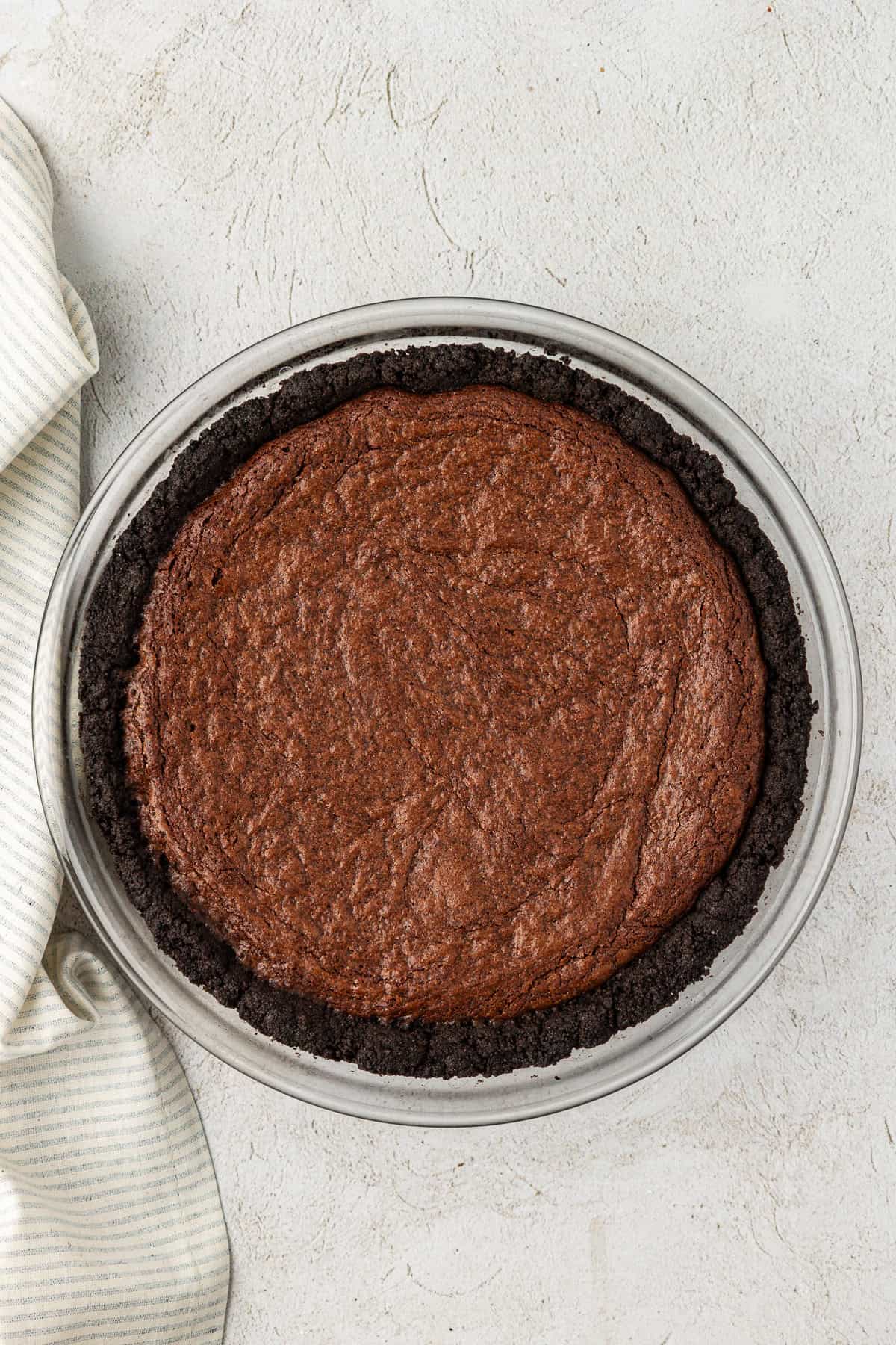a clear glass pie dish with oreo crust and a brownie layer baked in it
