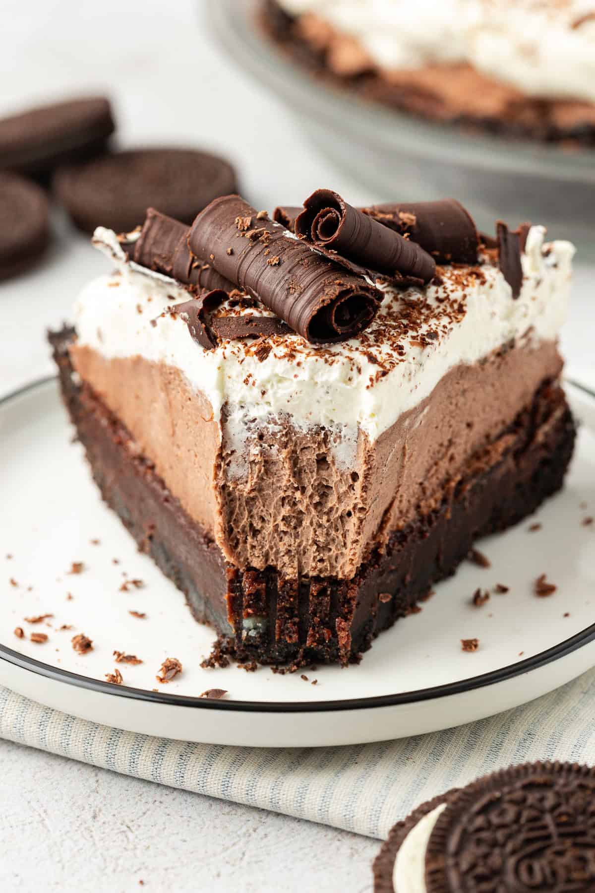 a slice of mud pie on a small white plate with a bite missing out of the tip of the pie and whole oreos scattered around