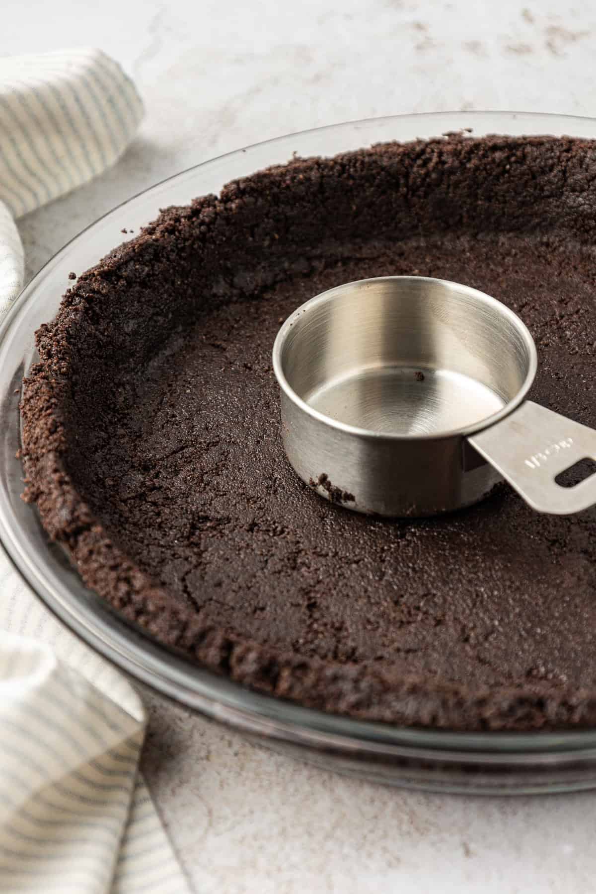 oreo crust pressed down into a class pie dish with a measuring cup