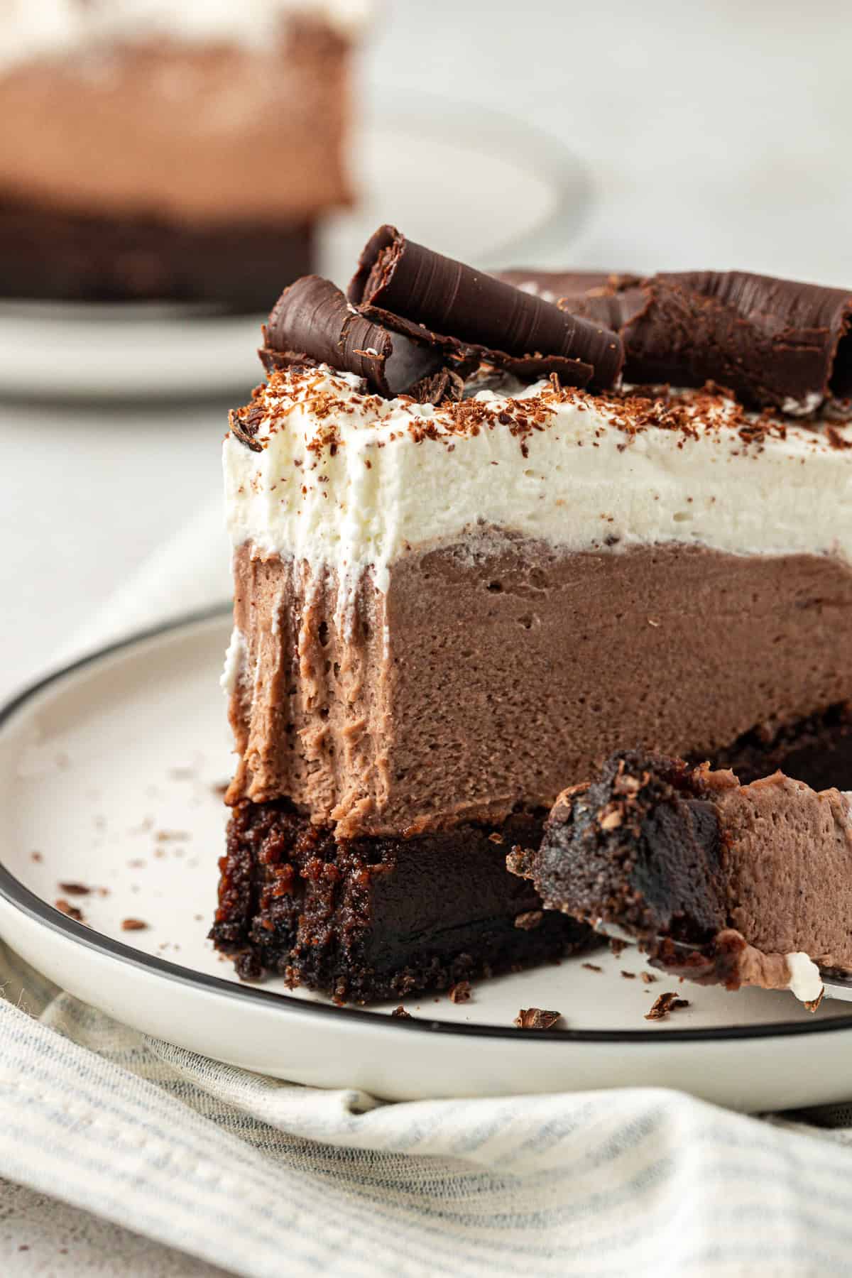 side view of a slice of mud pie on a white plate with a fork that has one bite out of the pie on it, leaning on the plate