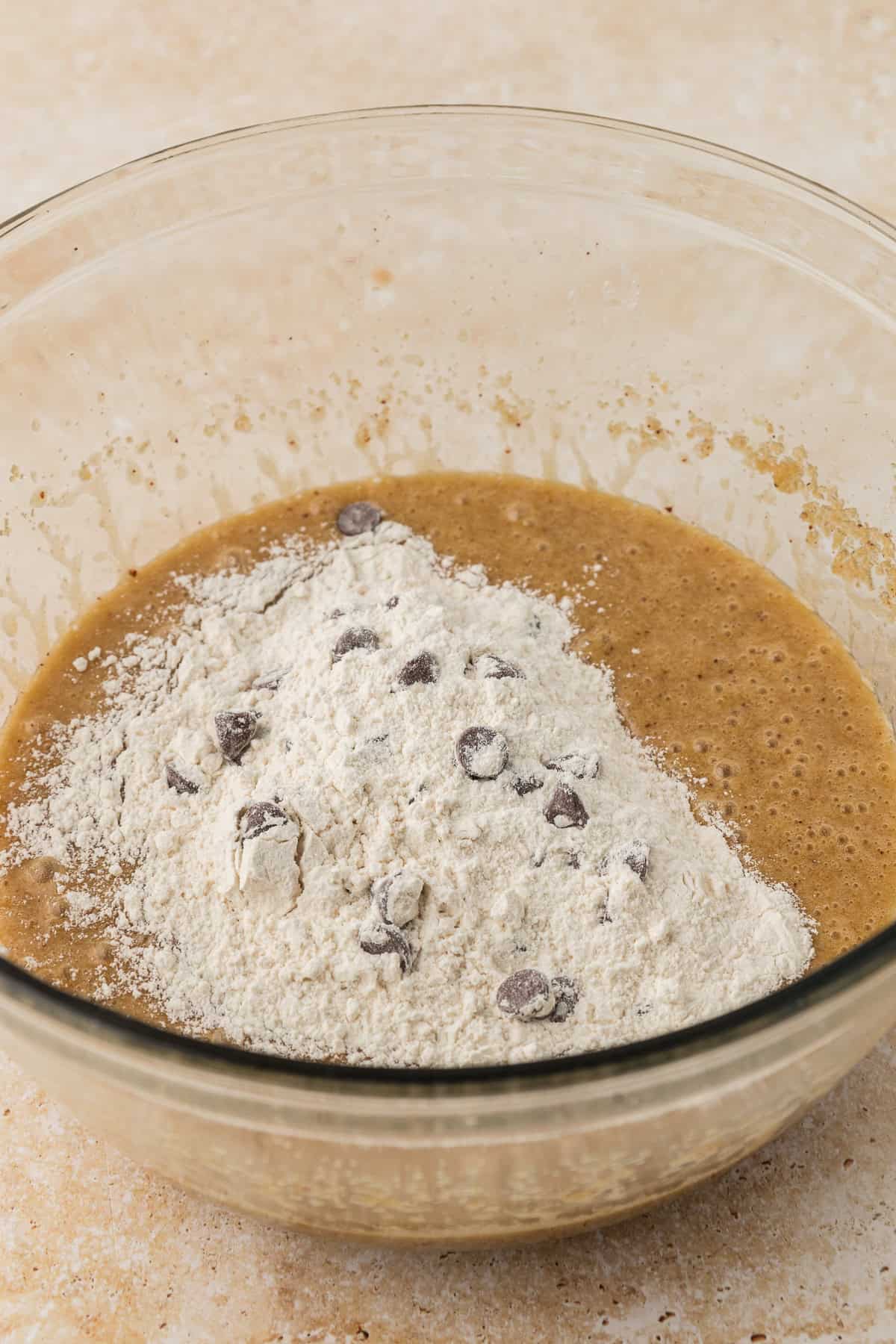 wet ingredients for pizookie with dry ingredients in a pile on top in a clear glass bowl