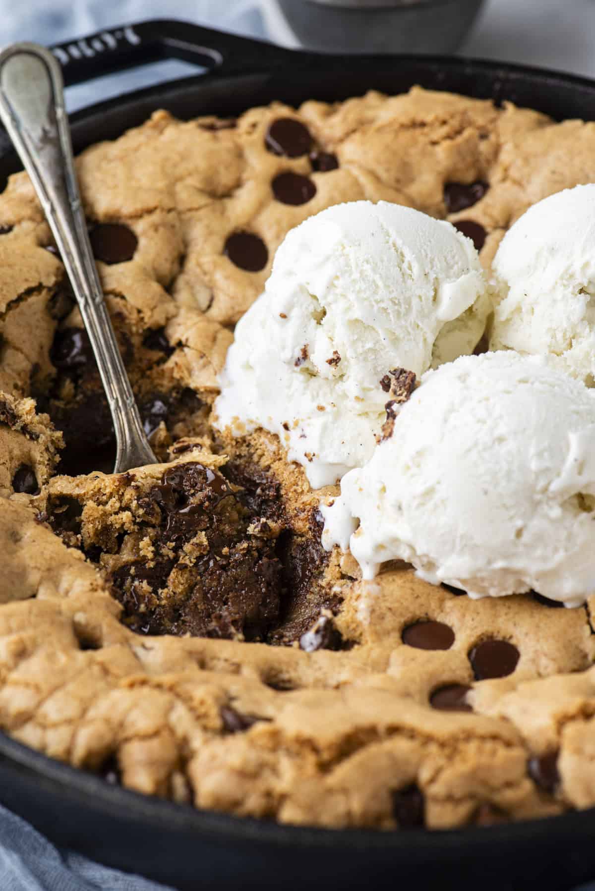 pizookie in a cast iron skillet with a spoon stick into it, bites missing and topped with three scoops of vanilla ice cream