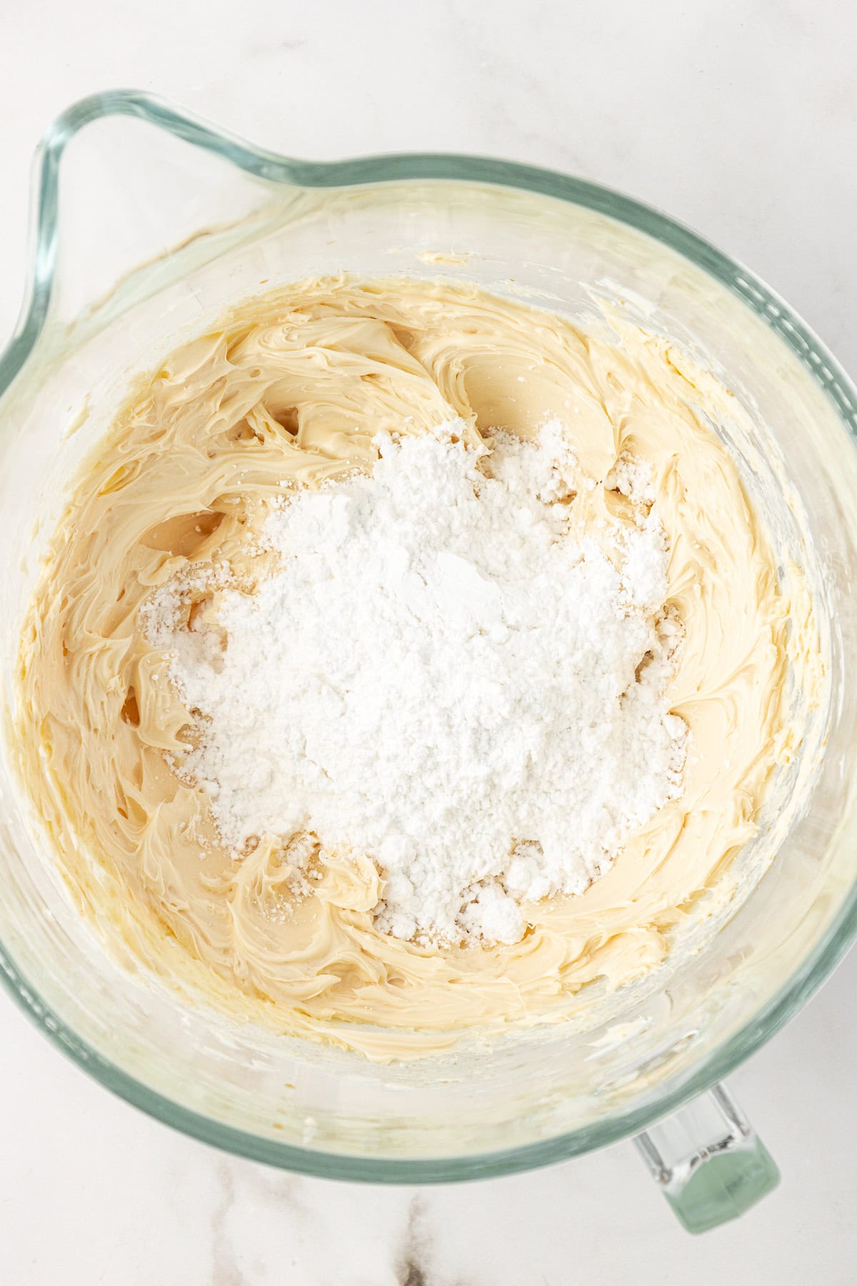 vanilla frosting ingredients mixed together with a pile of powdered sugar on top